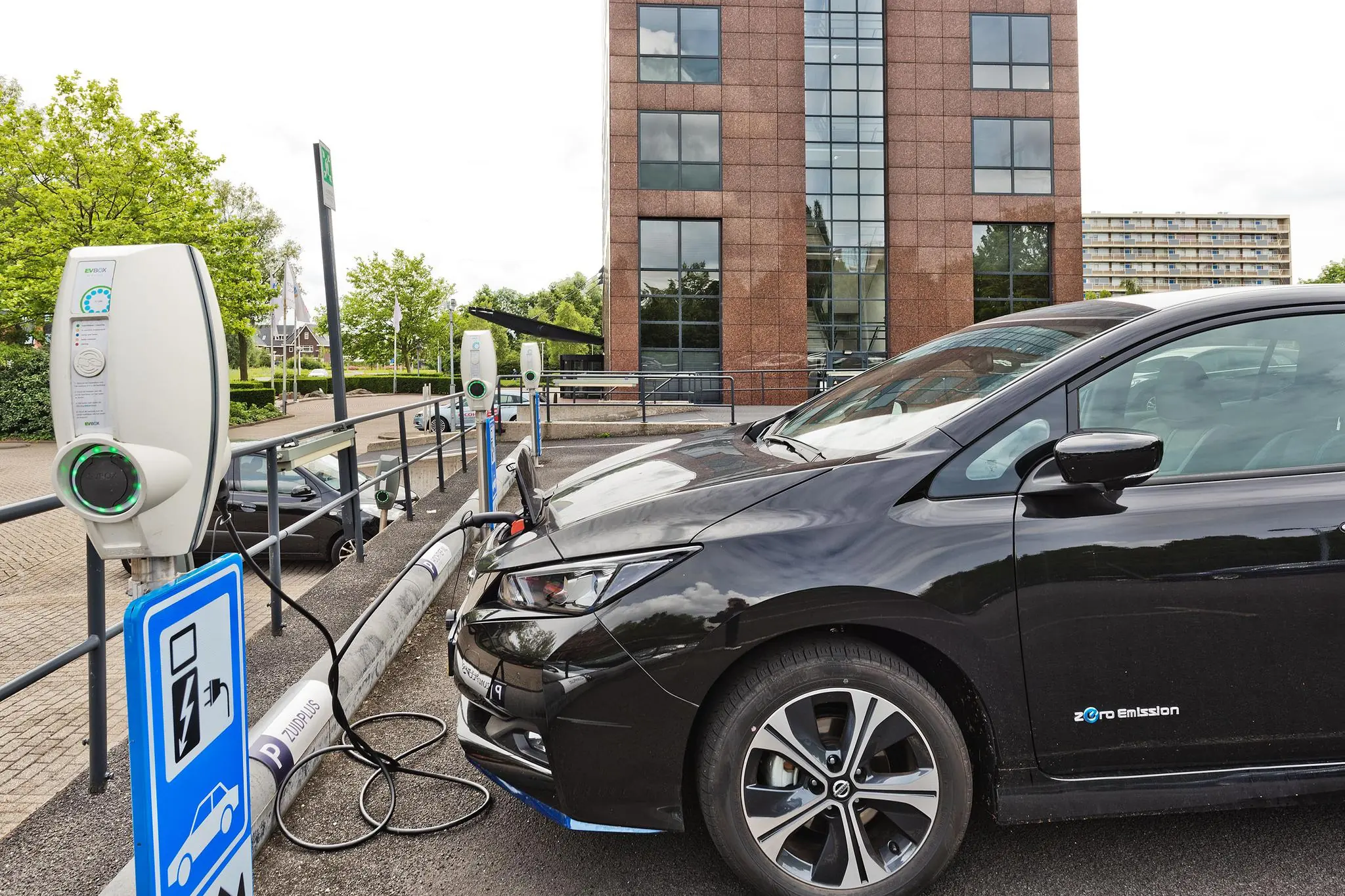 Zwarte elektrische auto laadt op bij laadpaal op parkeerplaats aan de Prof. W.H. Keesomlaan, met kantoorgebouw op de achtergrond.