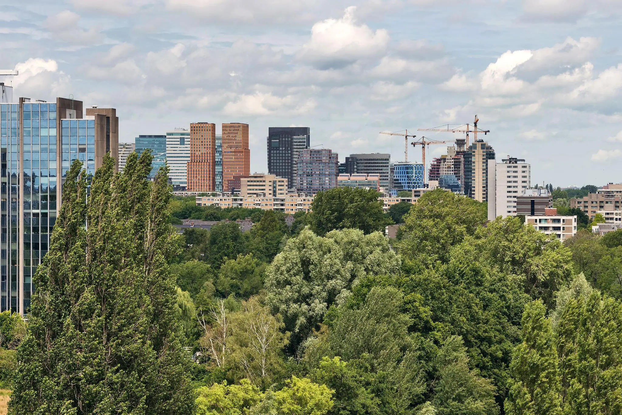 Uitzicht op de skyline van de Zuidas in Amsterdam met moderne kantoorgebouwen en veel groen op de voorgrond vanaf de Prof. W.H. Keesomlaan.