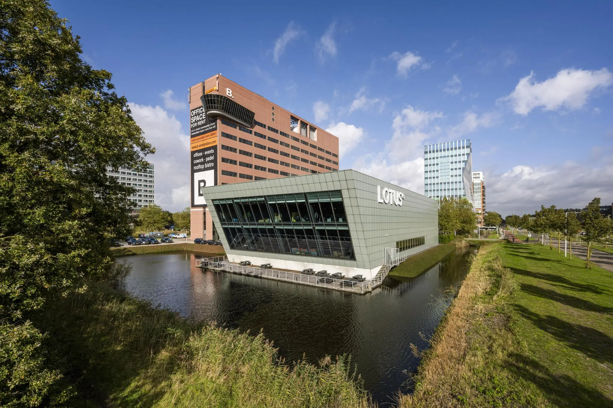 Modern kantoorgebouw 'Lotus' aan het water op de Johan Huizingalaan in Amsterdam, met op de achtergrond het grote B-Building bedrijfsverzamelgebouw.