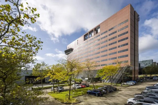 Modern kantoorgebouw aan de Johan Huizingalaan in Amsterdam met parkeerplaats en bomen op de voorgrond.
