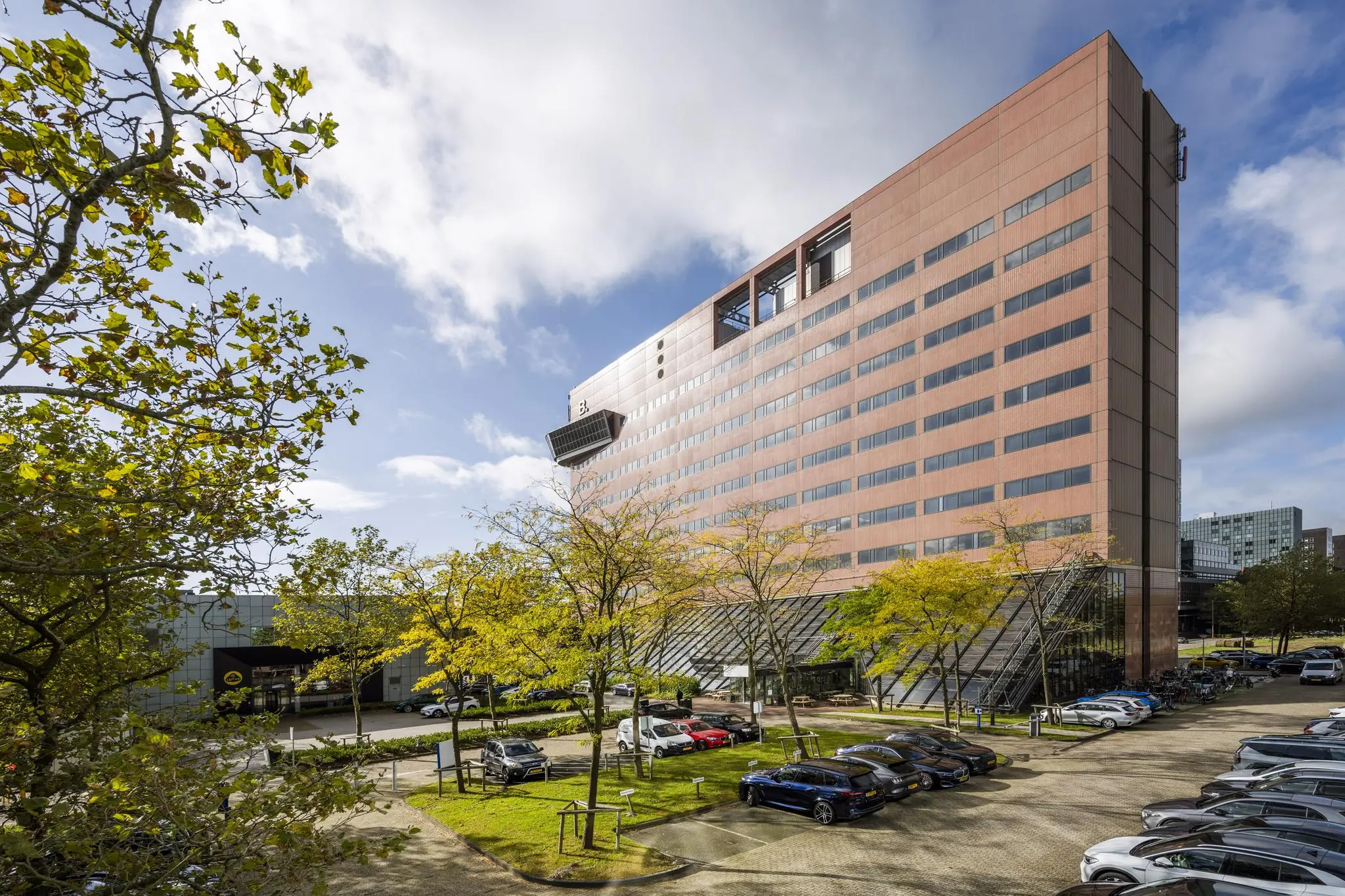 Modern kantoorgebouw aan de Johan Huizingalaan in Amsterdam met parkeerplaats en bomen op de voorgrond.