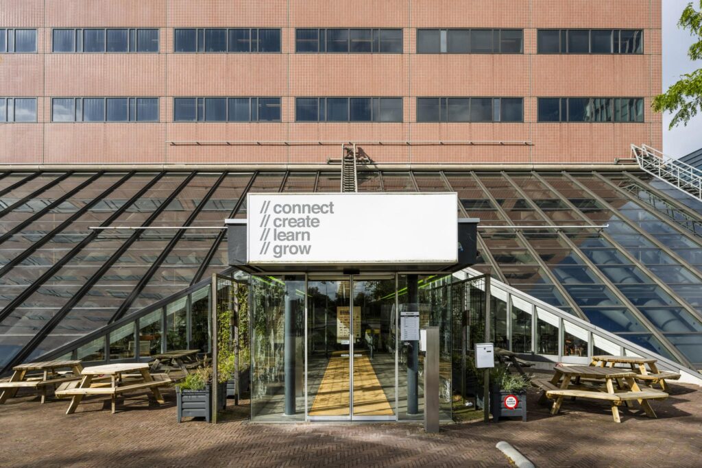 Ingang van een modern kantoorgebouw aan de Johan Huizingalaan met glazen gevel en de tekst "connect, create, learn, grow" boven de entree.