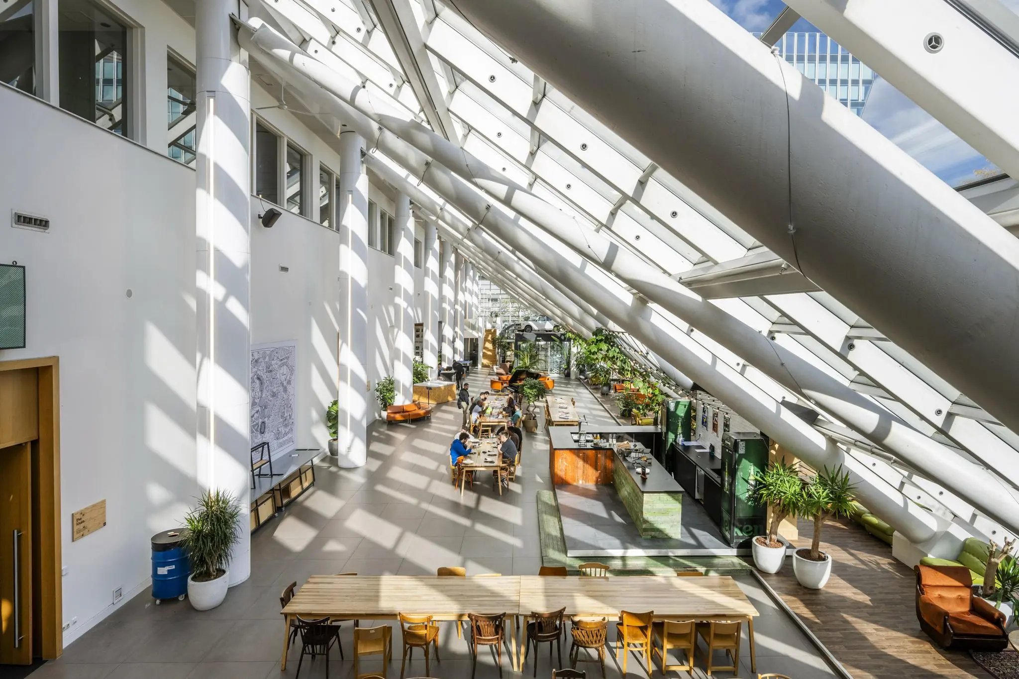 Lichte en moderne binnentuin met glazen dak, grote planten, zitplekken en een open werkruimte aan de Johan Huizingalaan.