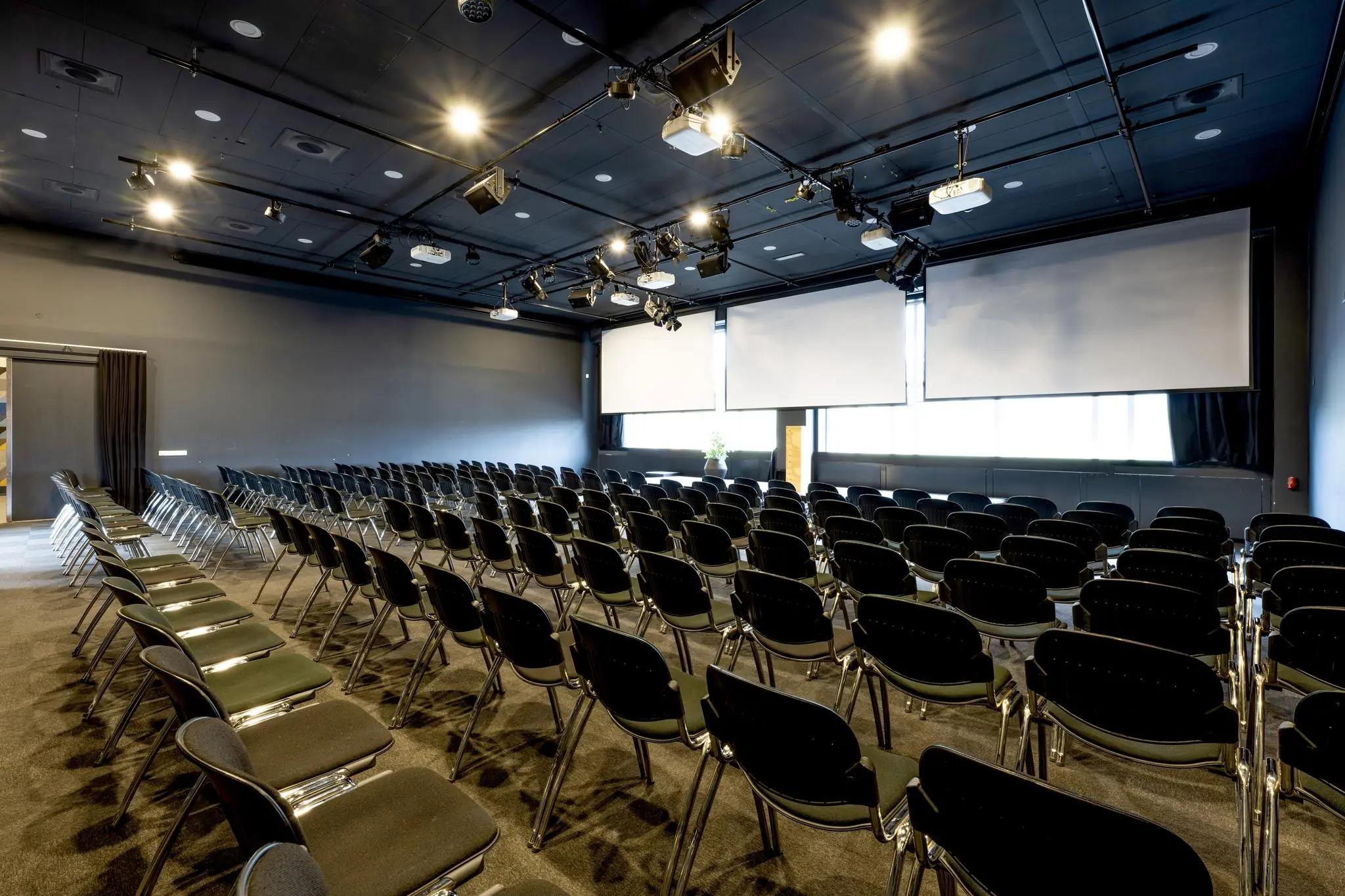 Moderne conferentieruimte aan de Johan Huizingalaan met rijen stoelen, projectieschermen en plafondverlichting.