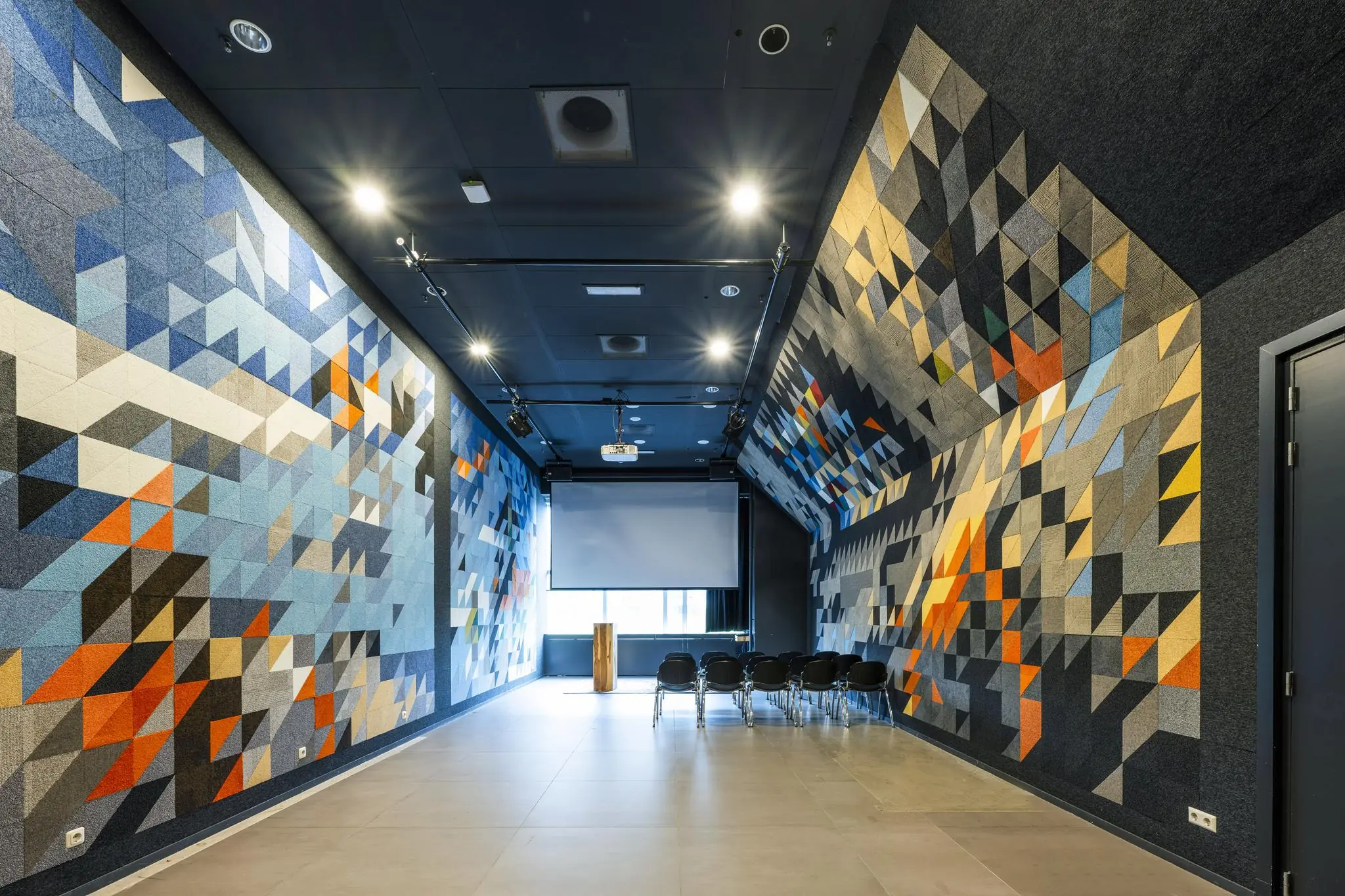 Moderne presentatieruimte aan de Johan Huizingalaan met kleurrijke geometrische wandpanelen, een projector en opgestelde stoelen.