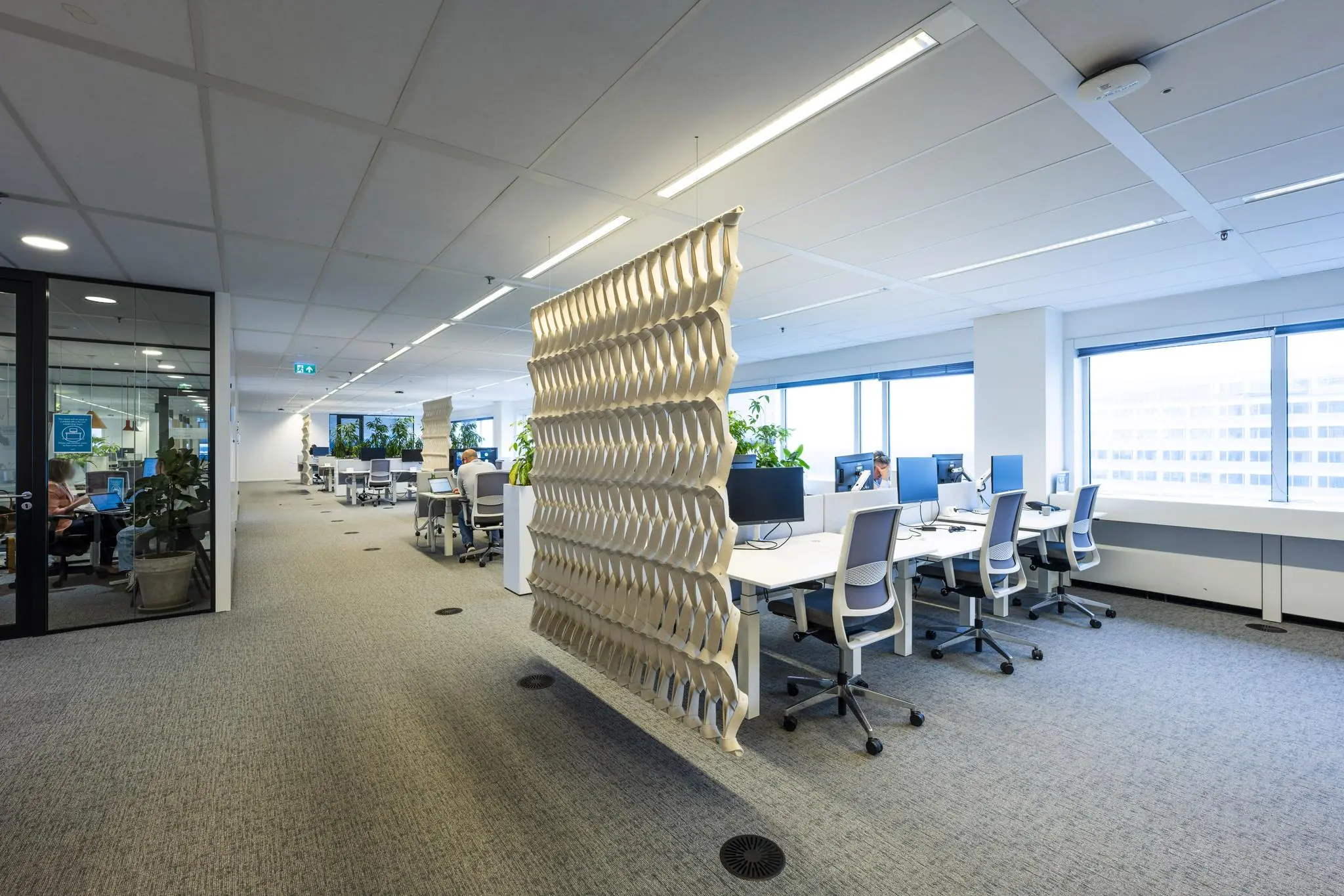 Modern kantoorinterieur aan de Johan Huizingalaan met open werkplekken, glazen vergaderruimte en een decoratieve ruimteverdeler.