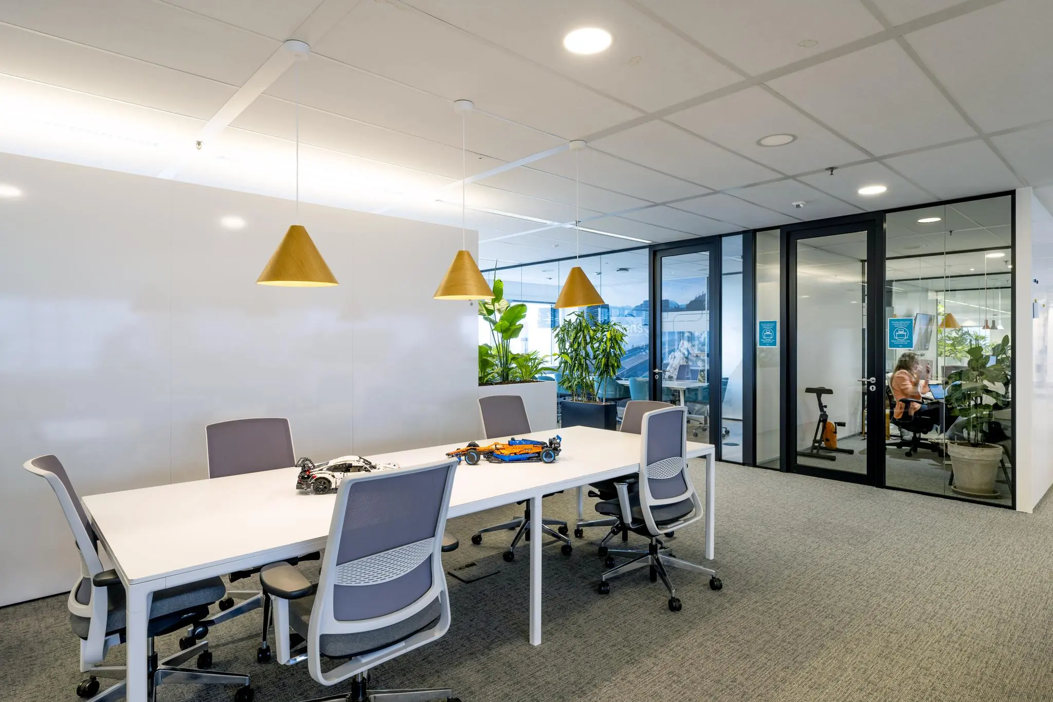 Moderne vergaderruimte aan de Johan Huizingalaan met een grote witte tafel, grijze stoelen, hanglampen en glazen kantoren op de achtergrond.
