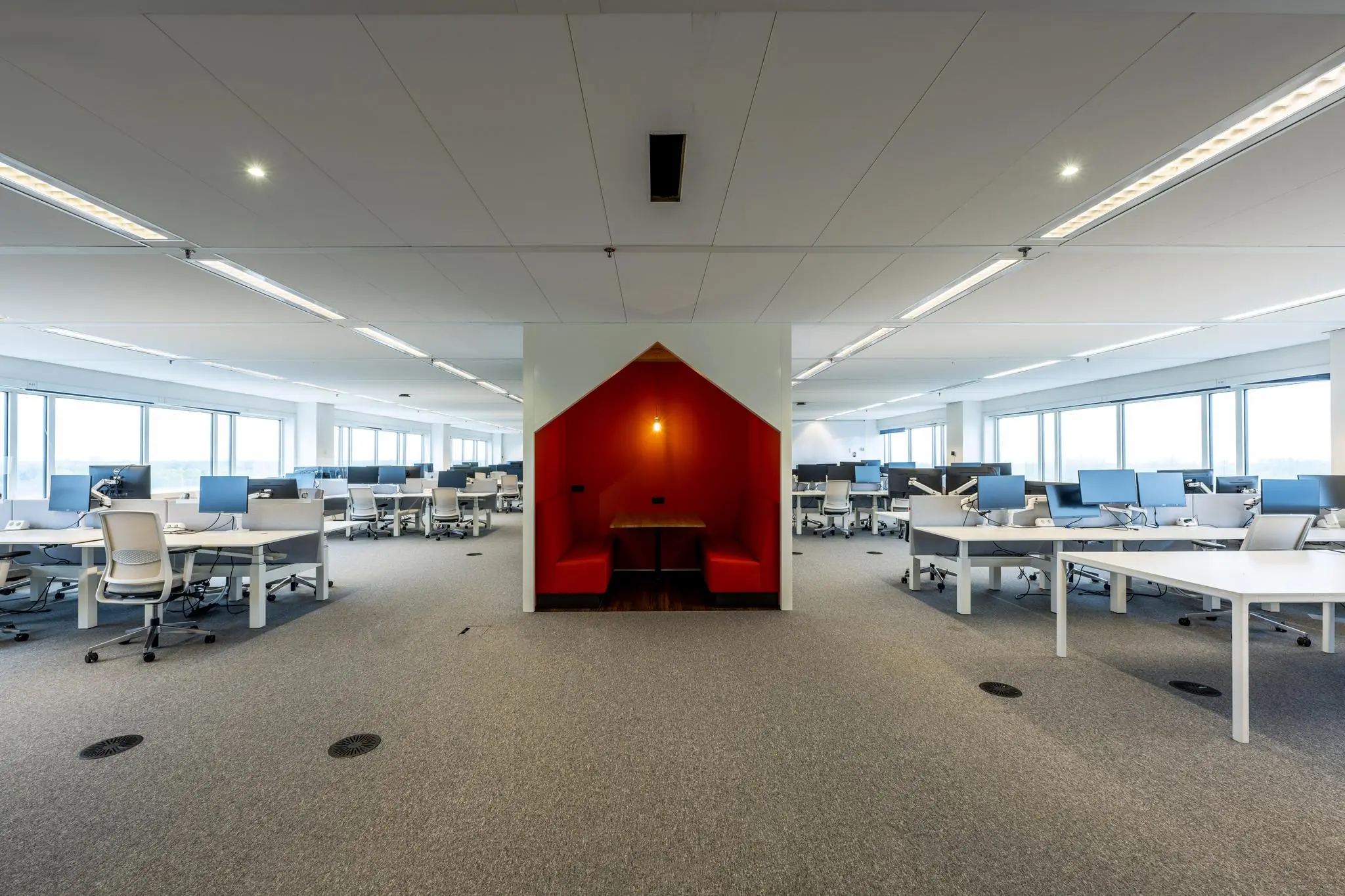 Ruim en modern kantoorlanschap aan de Johan Huizingalaan met open werkplekken en een opvallende rode zitnis voor overleg.