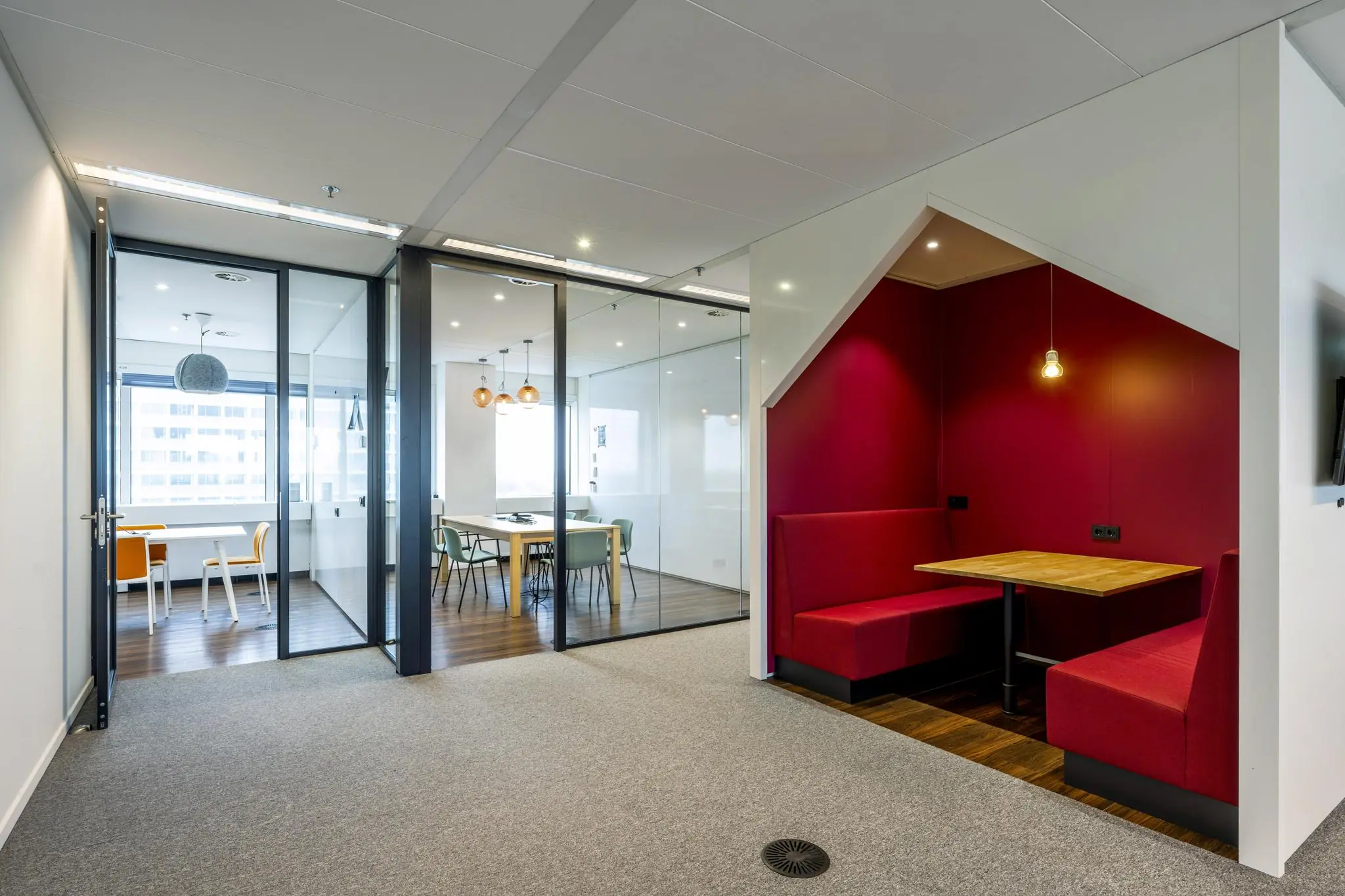 Moderne kantoorruimte aan de Johan Huizingalaan met glazen vergaderruimtes en een knusse zitnis met rode wanden en houten tafel.