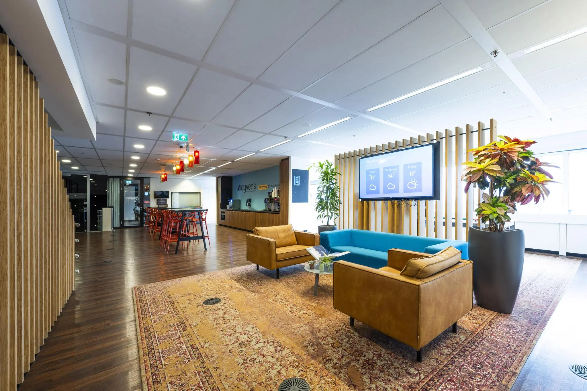 Moderne kantoorlounge aan de Johan Huizingalaan met zithoek, groot scherm en planten in een lichte en open ruimte.