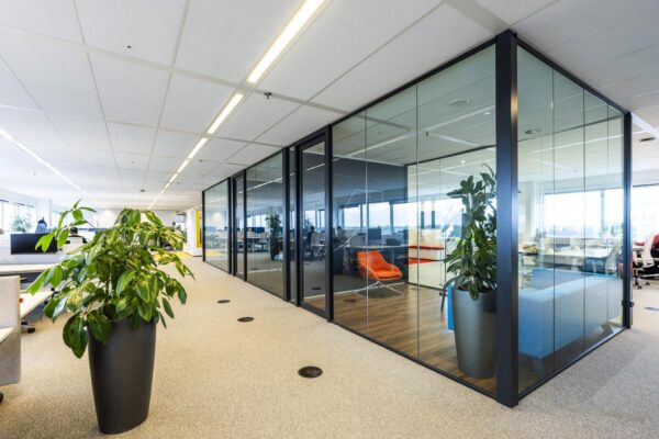 Modern kantoorinterieur aan de Johan Huizingalaan met glazen vergaderruimtes, felgekleurde meubels en grote planten.