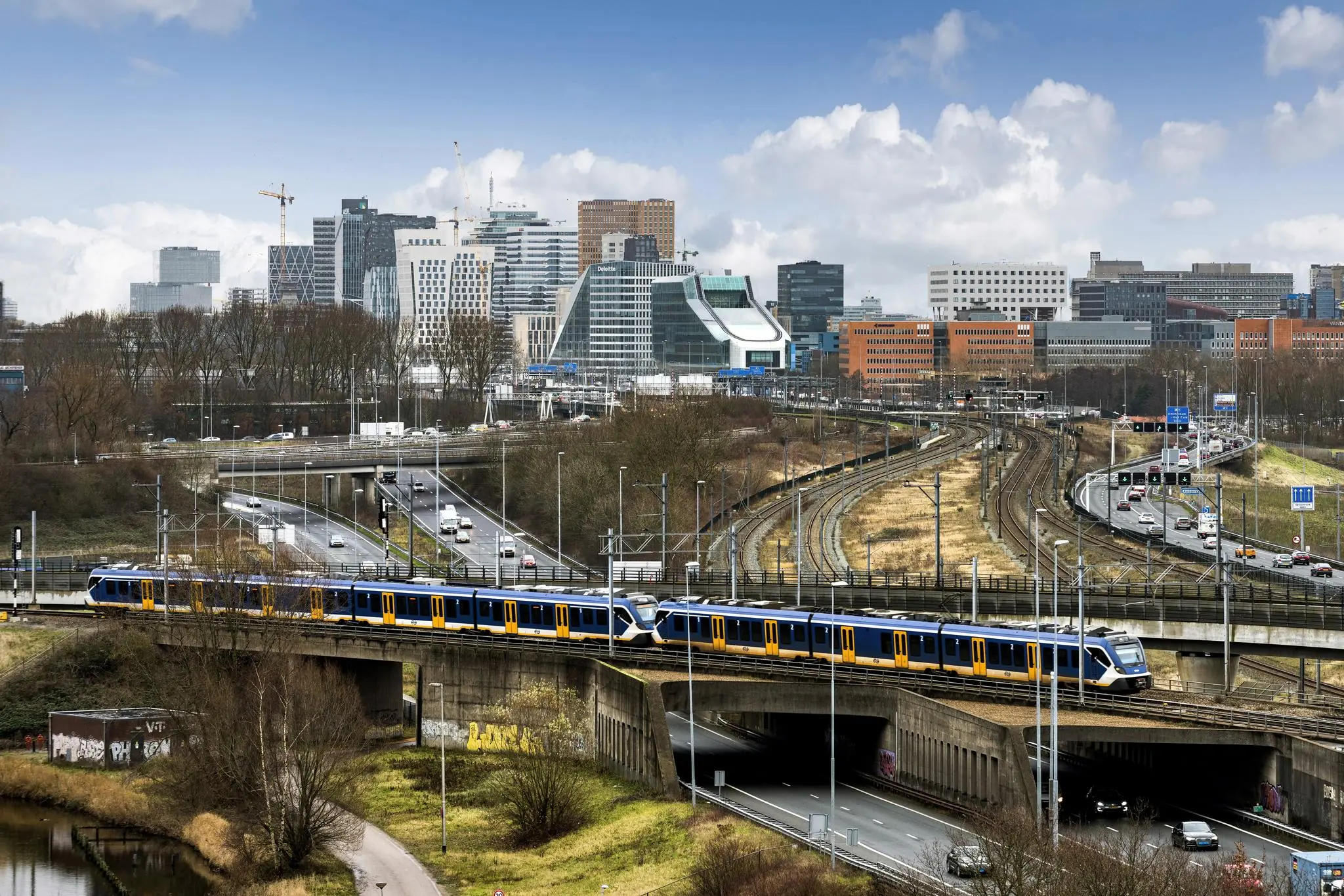 Een intercitytrein rijdt over een viaduct bij de Johan Huizingalaan met de skyline van Amsterdam-Zuid op de achtergrond.