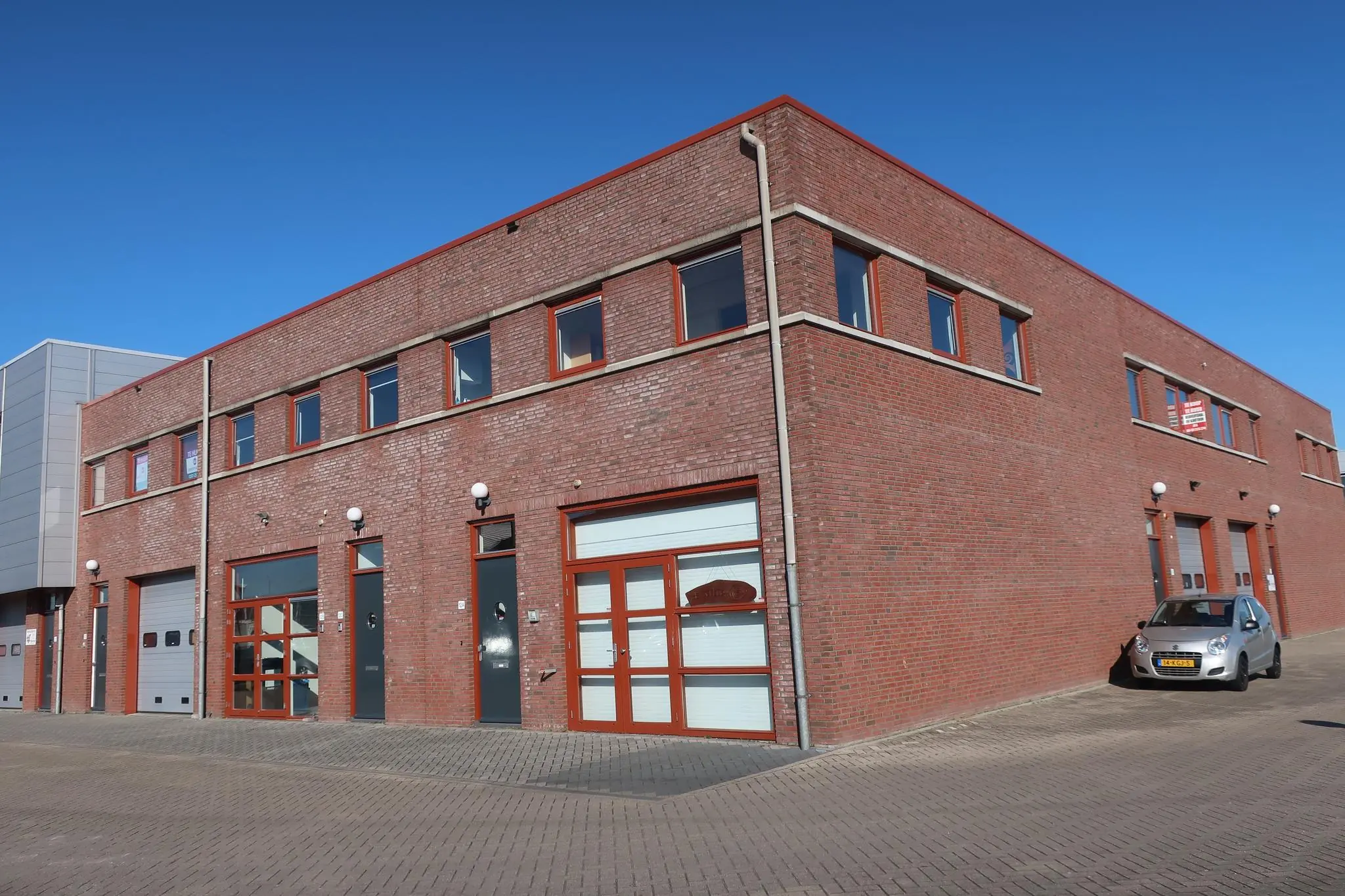 Bakstenen bedrijfsverzamelgebouw aan De Corridor met meerdere units en een geparkeerde auto op de hoek.