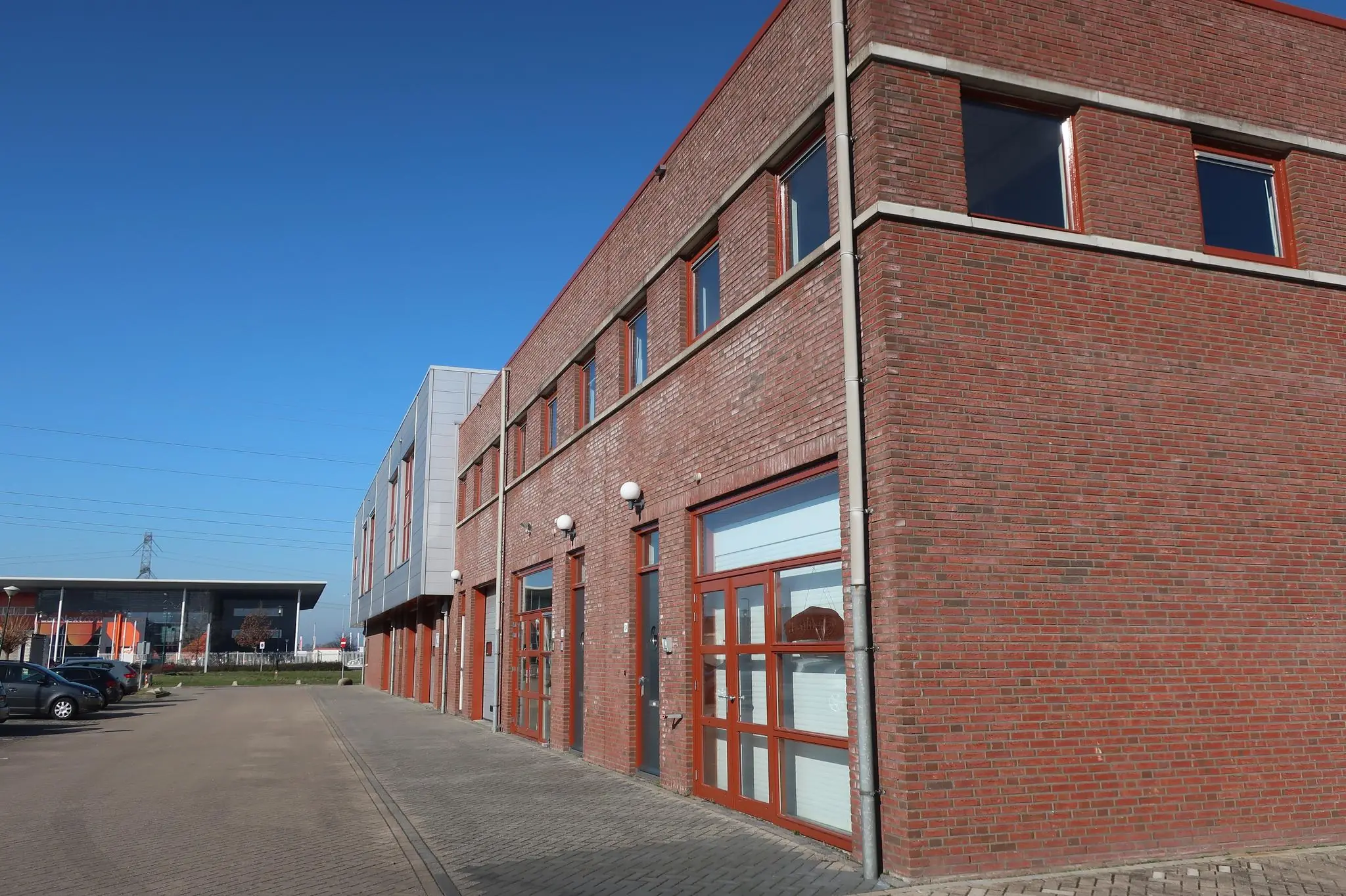 Bakstenen bedrijfsverzamelgebouw aan De Corridor met rode kozijnen en parkeervakken langs de weg.