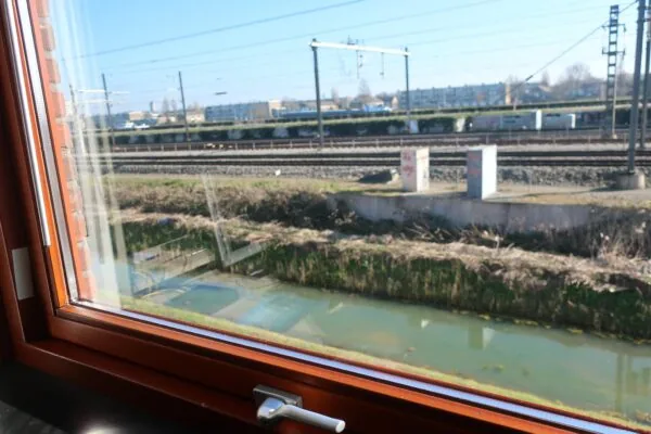 Uitzicht vanuit een raam op het spoor bij De Corridor, met een sloot op de voorgrond en treinrails op de achtergrond.