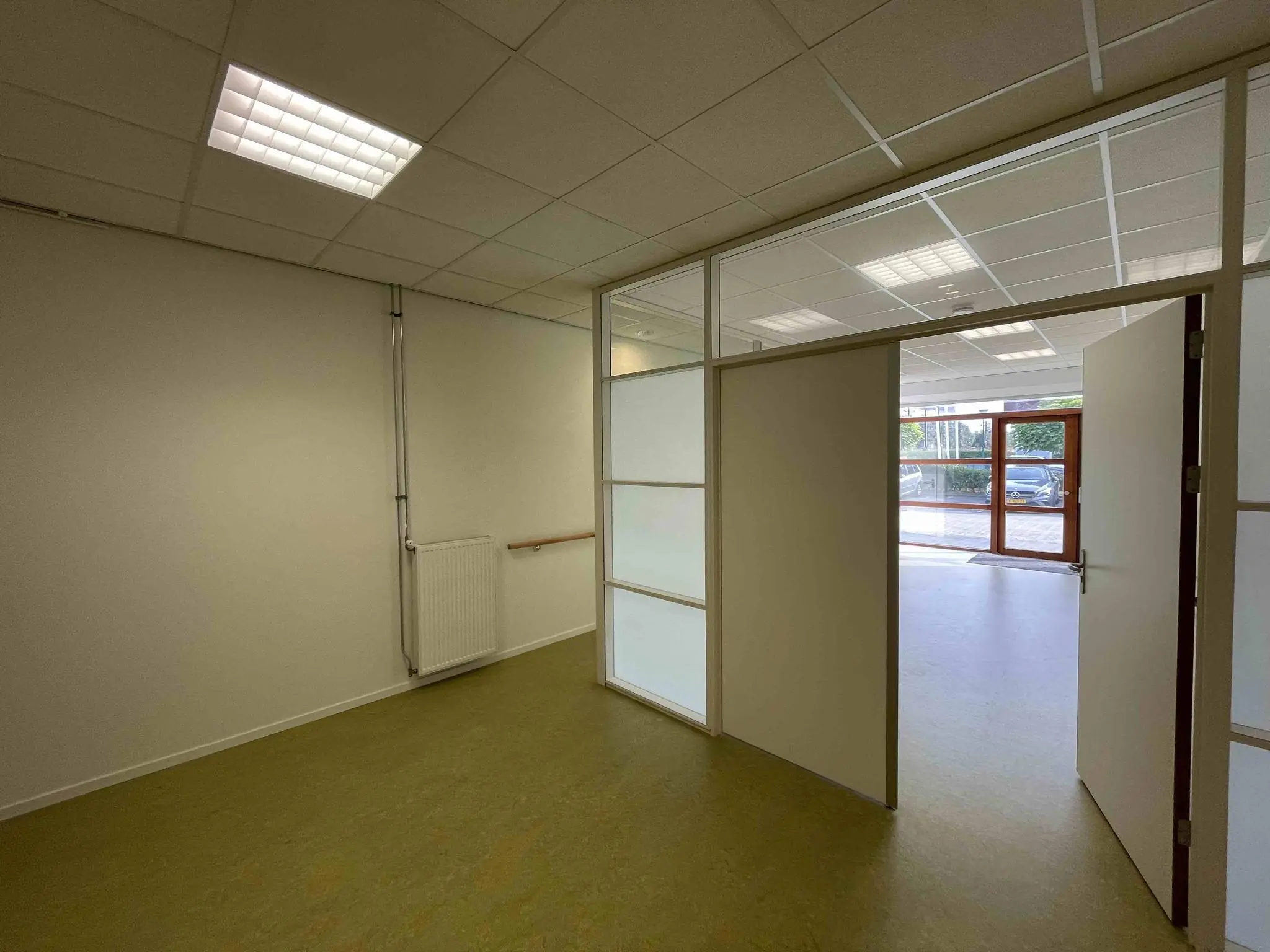 Interieur van een lege ruimte in De Corridor met open deur naar een lichte hal en buitenzicht.