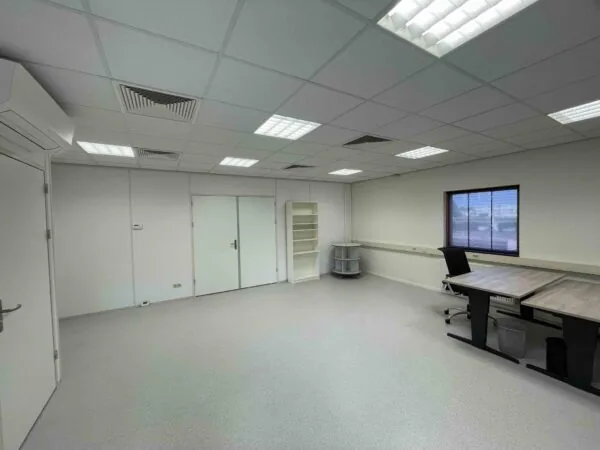 Kantoorruimte in De Corridor met bureaus, een stoel, opbergmeubels en een raam met zonwering.