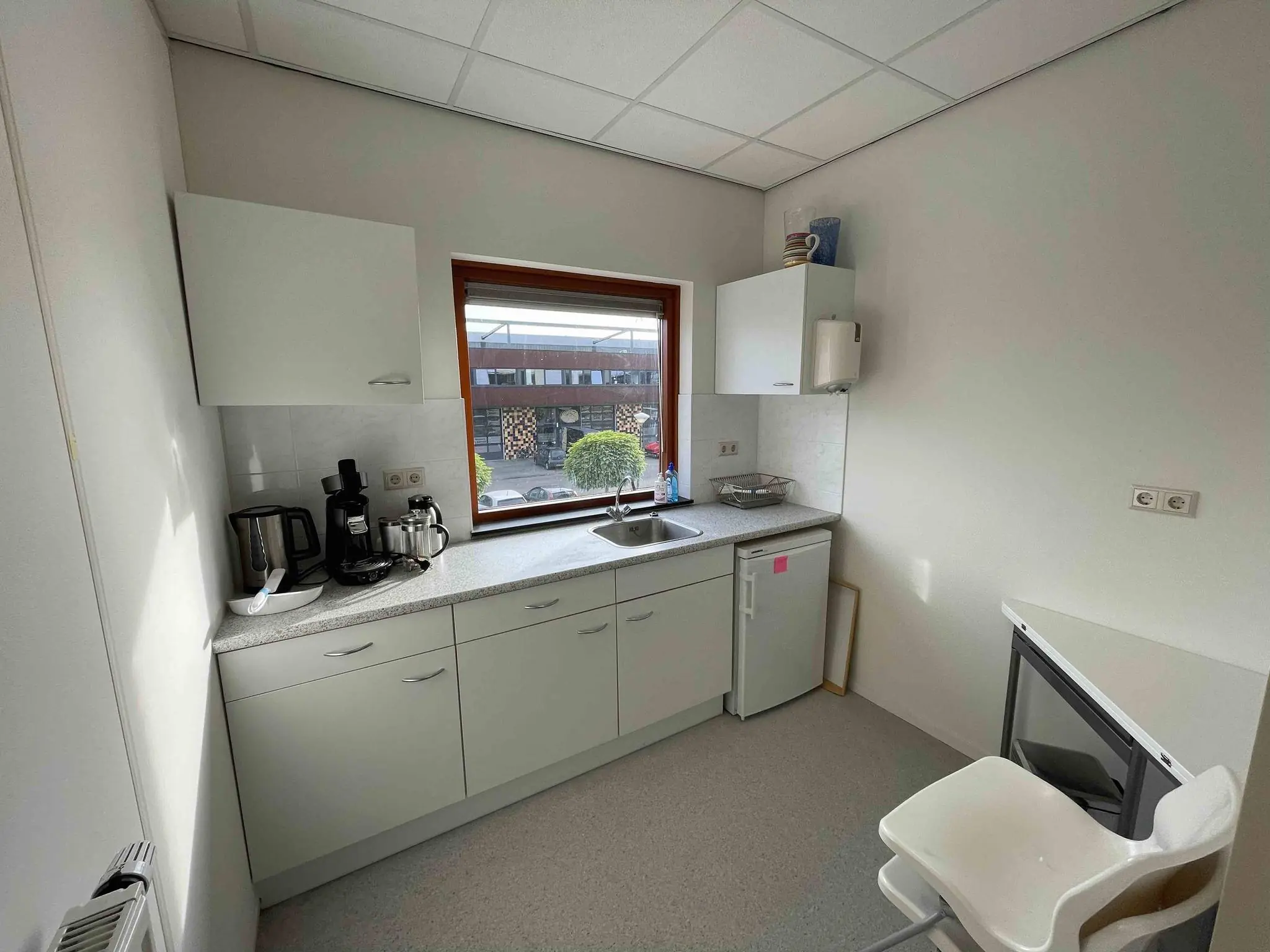 Kleine pantry met aanrecht, koffiezetapparaat en raam met uitzicht op de straat bij De Corridor.