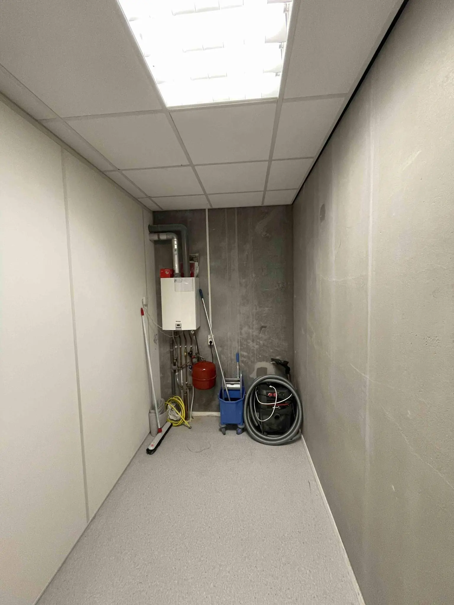 Kleine onderhoudsruimte in De Corridor met schoonmaakspullen, een cv-ketel en een stofzuiger.