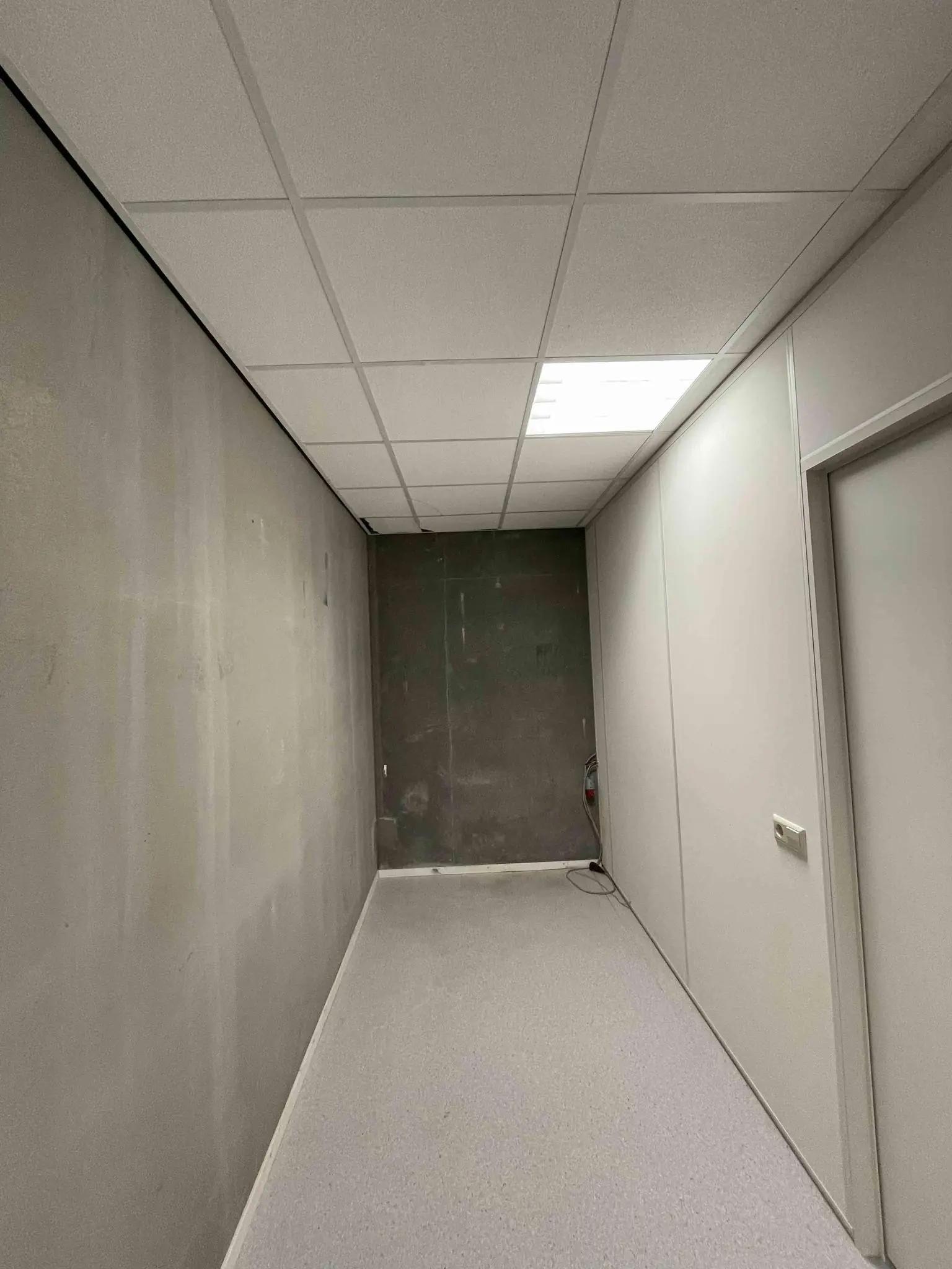 Kale gang met systeemplafond, grijze vloer en onafgewerkte achterwand in De Corridor.