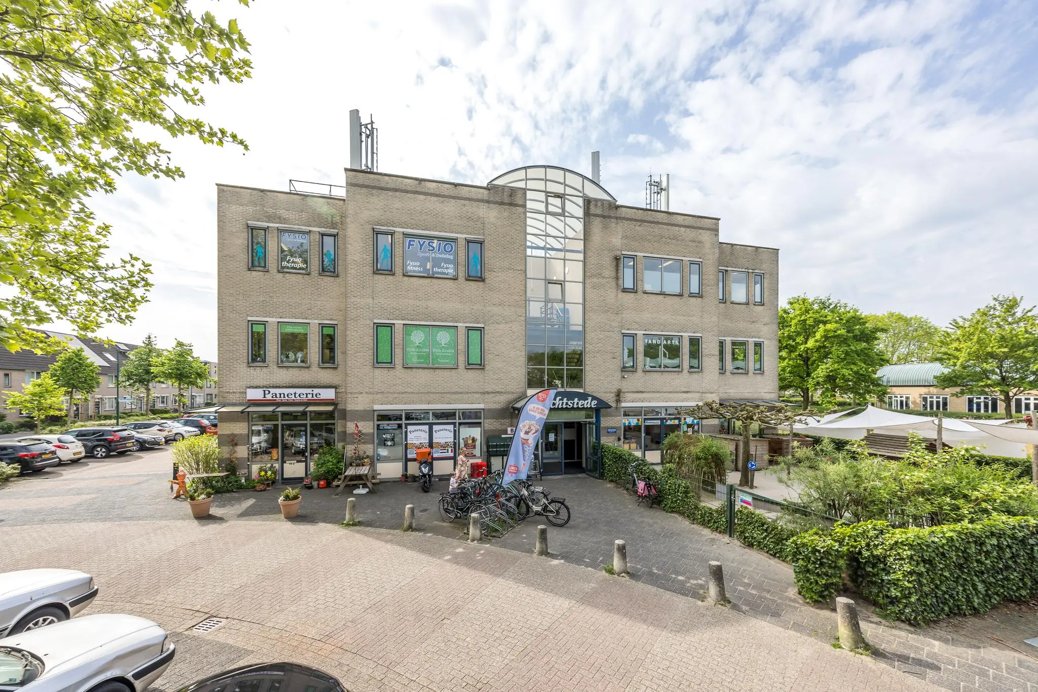 Vooraanzicht van een modern bedrijfsverzamelgebouw aan de Buitenweg met onder andere een fysiopraktijk, lunchroom en winkels.