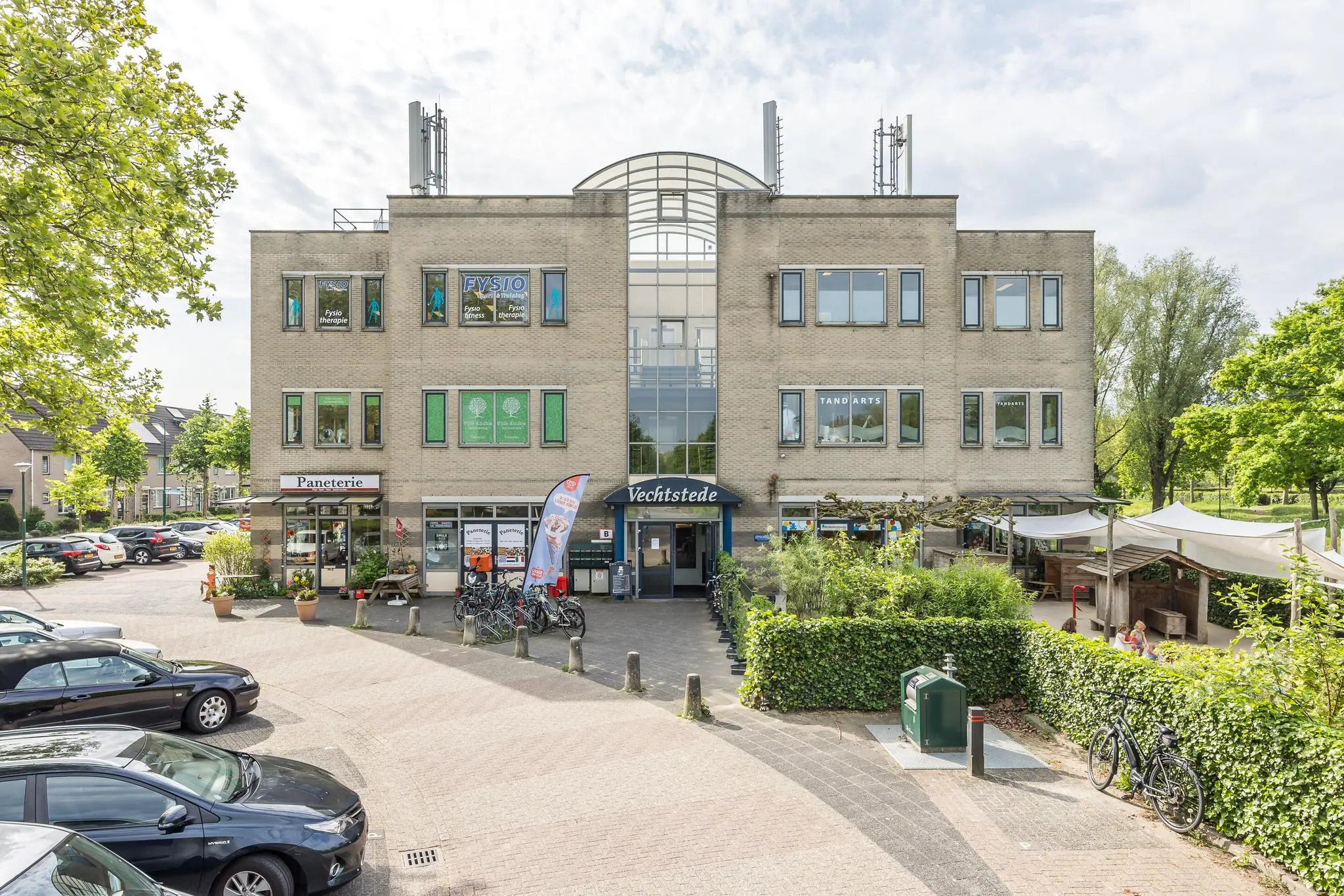 Vooraanzicht van het gebouw Vechtsstede aan de Buitenweg, met verschillende praktijken en winkels zoals een tandarts, fysiotherapie, paneterie en buitenterras.