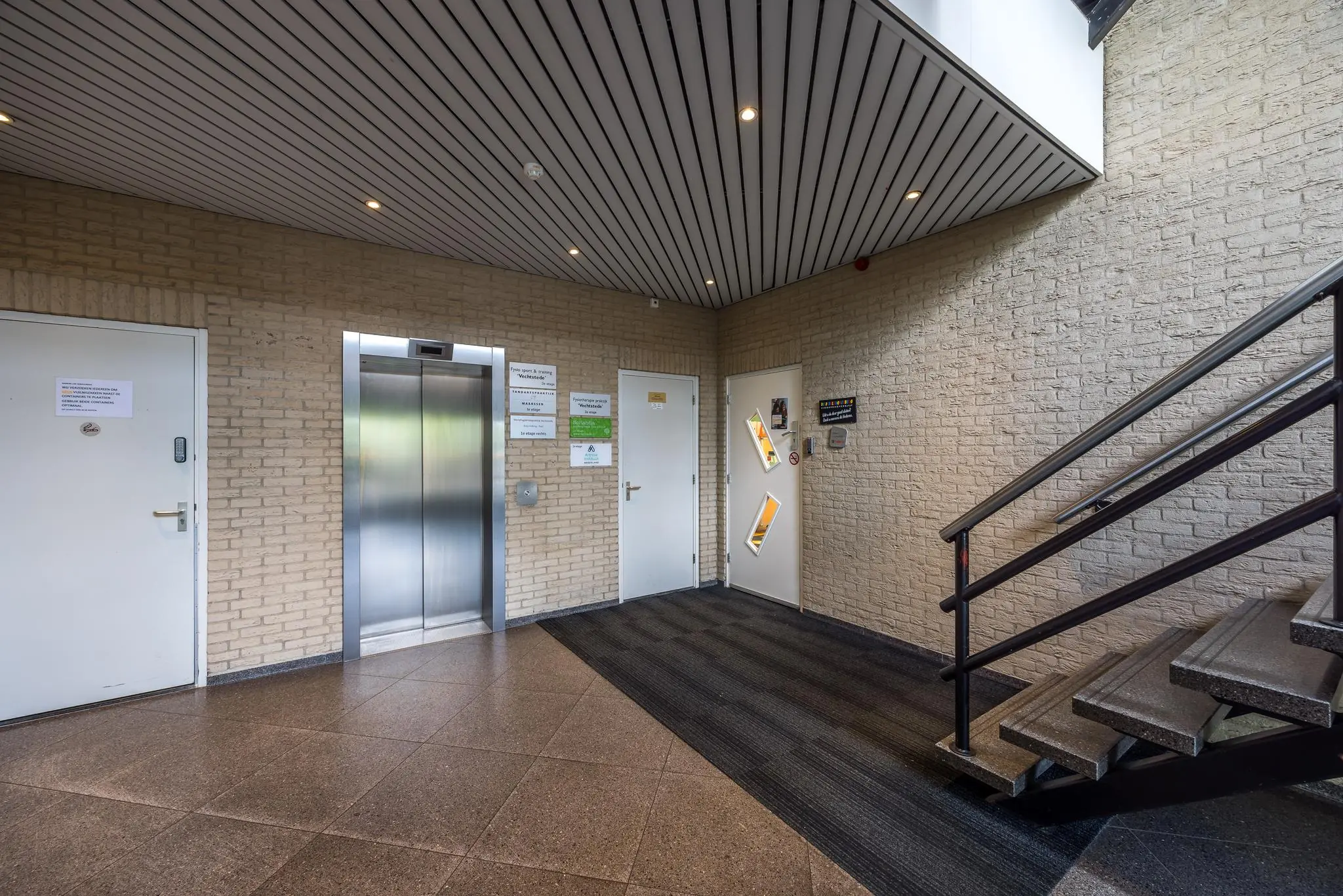 Entreehal met een lift, meerdere deuren en een trap in een gebouw aan de Buitenweg.