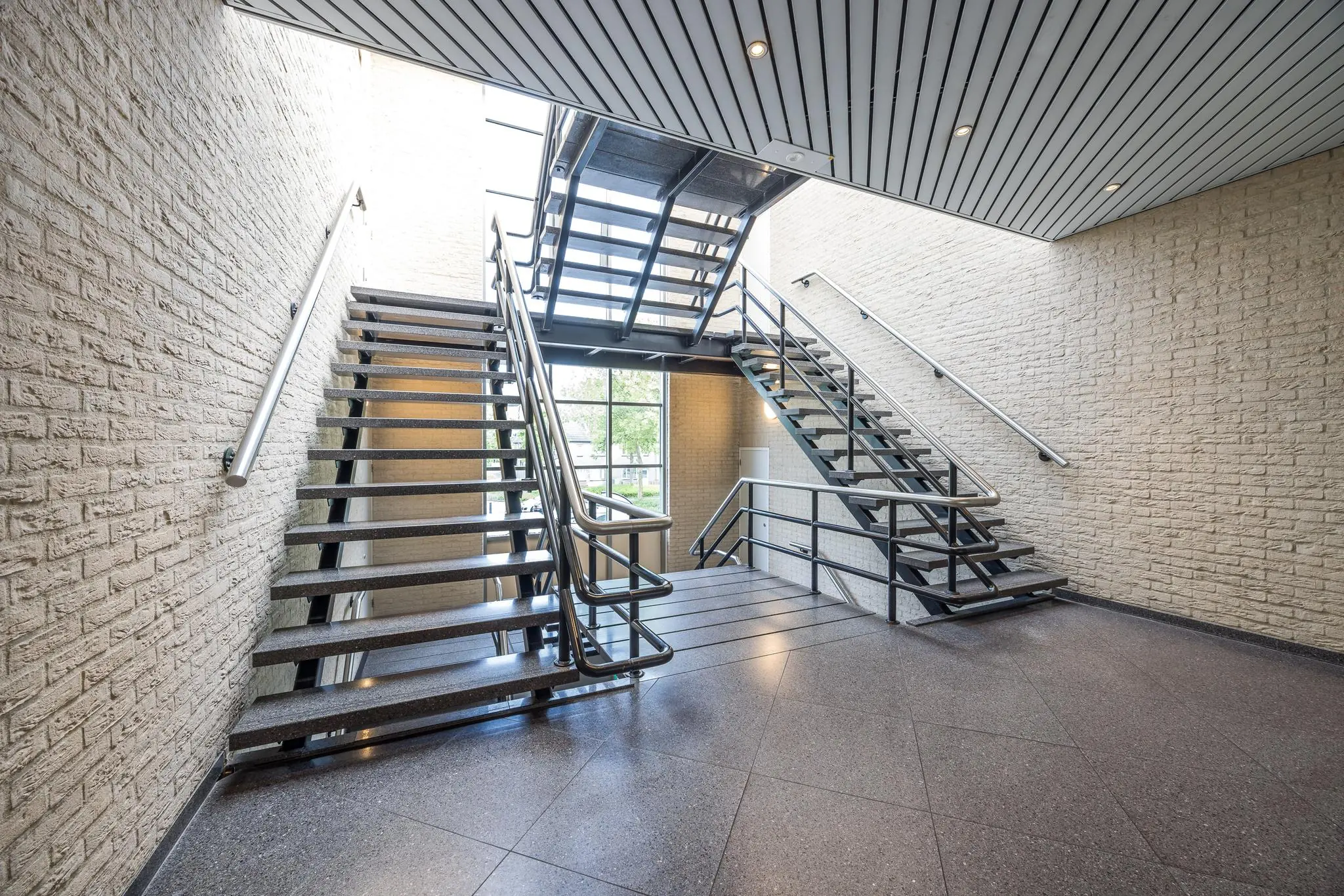 Moderne trapopgang met stalen leuningen en tegelvloer in gebouw aan de Buitenweg.