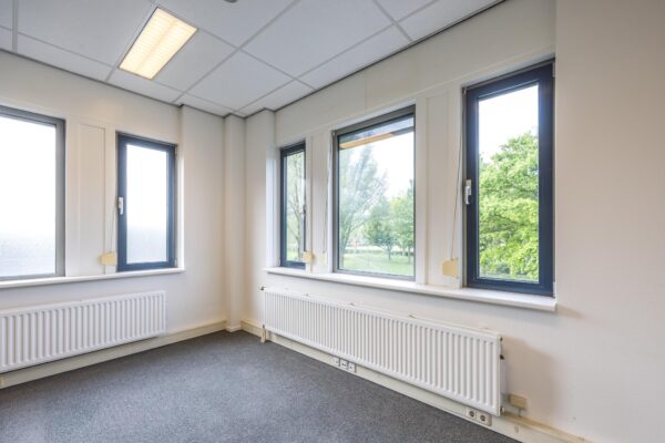 Licht kantoorhoekje met meerdere ramen, radiatoren en uitzicht op groen aan de Buitenweg.