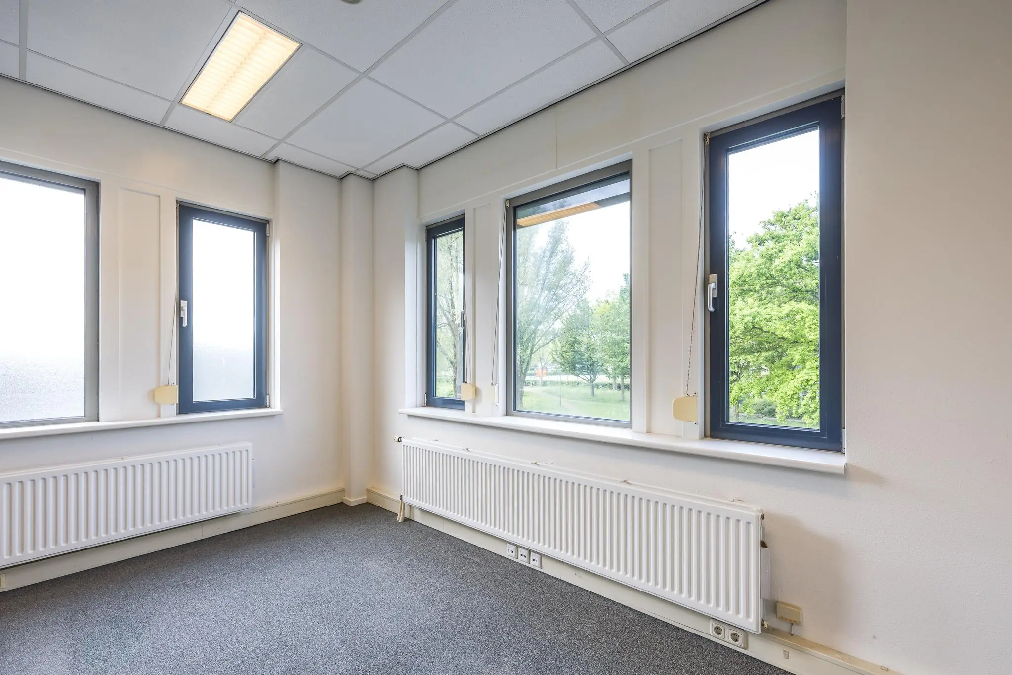 Licht kantoorhoekje met meerdere ramen, radiatoren en uitzicht op groen aan de Buitenweg.
