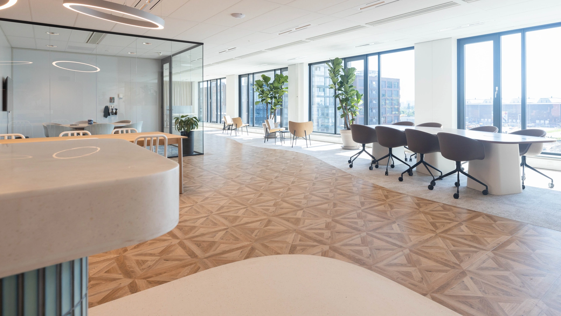 Modern kantoorinterieur aan de Mt. Lincolnweg met grote ramen, vergadertafel, loungezitjes en houten visgraatvloer.