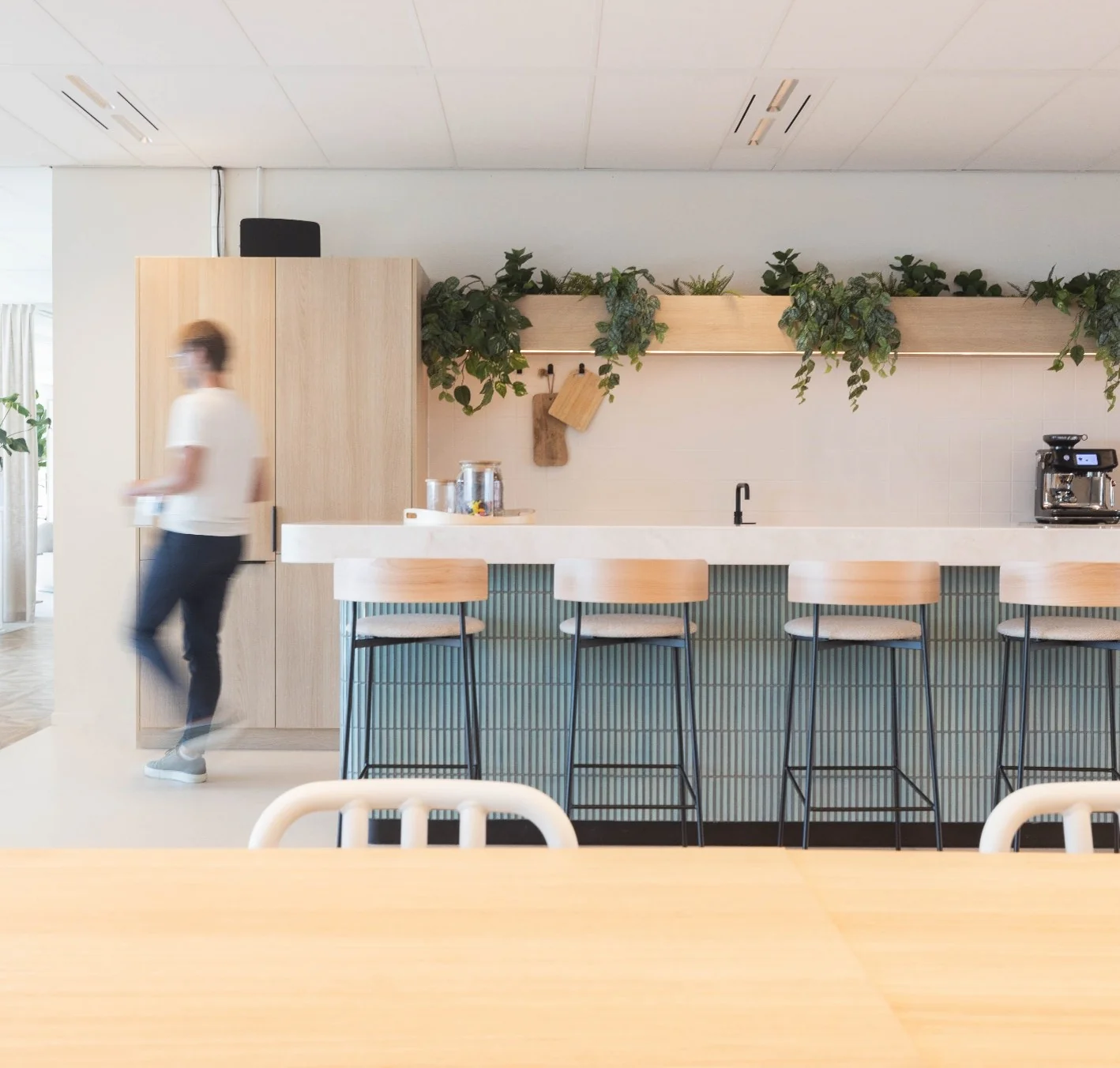 Moderne kantoorkeuken op Mt. Lincolnweg met houten elementen, barkrukken, hangplanten en een persoon in beweging.