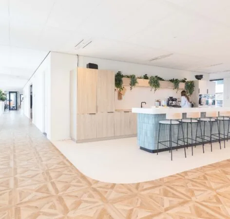 Moderne kantoorkeuken aan de Mt. Lincolnweg met een houten vloer, een bar met krukken en een vrouw bij het koffieapparaat.