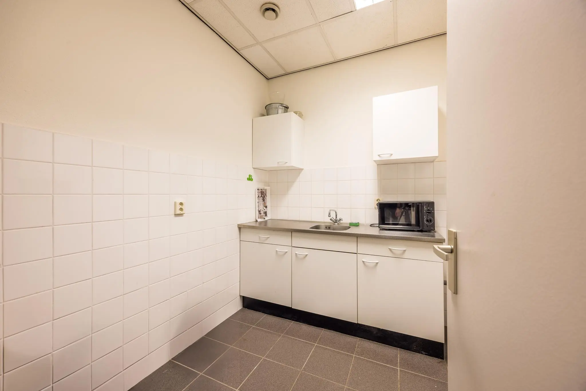 Kleine, eenvoudige pantrykeuken met witte kasten, een magnetron en een spoelbak op een grijs aanrecht.