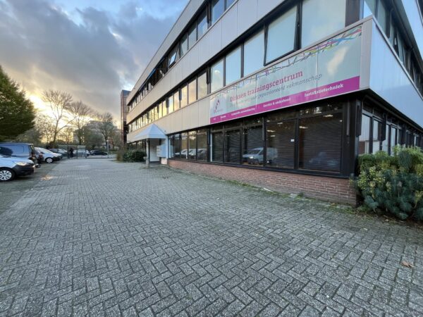 Vooraanzicht van het Dirksen trainingscentrum aan de Industrieweg met parkeerplaatsen en een ondergaande zon op de achtergrond.