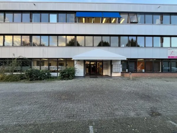 Ingang van het kantoorgebouw aan de Industrieweg met witte gevel en blauwe zonwering.