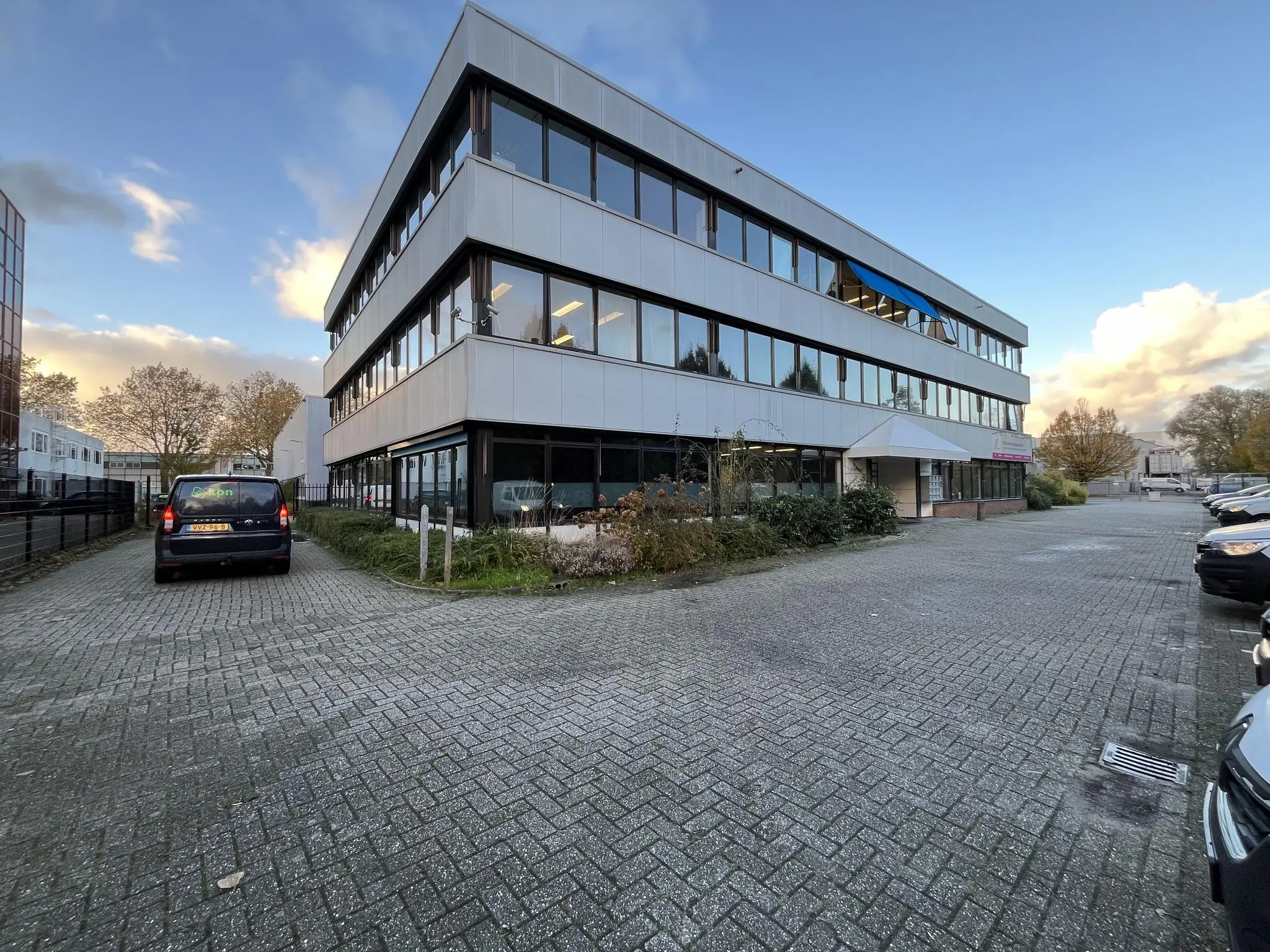 Kantoorpand aan de Industrieweg met parkeerplaatsen en geparkeerde auto's op een deels bewolkte dag.