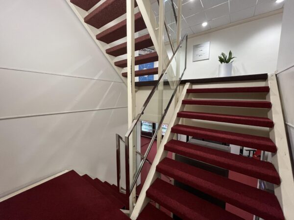 Trap met rode vloerbedekking en glazen leuning in een kantoorruimte aan de Industrieweg.