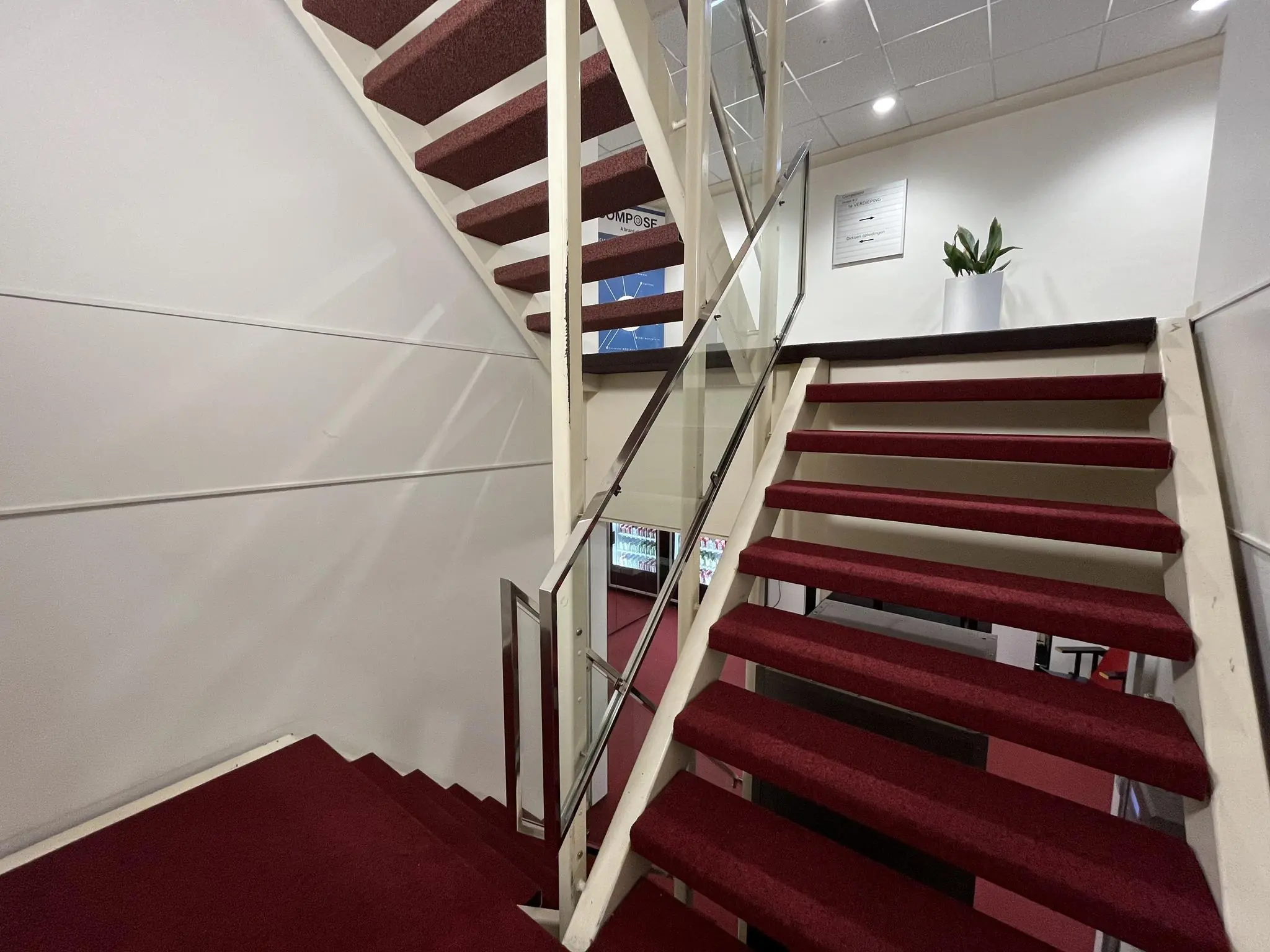 Trap met rode vloerbedekking en glazen leuning in een kantoorruimte aan de Industrieweg.
