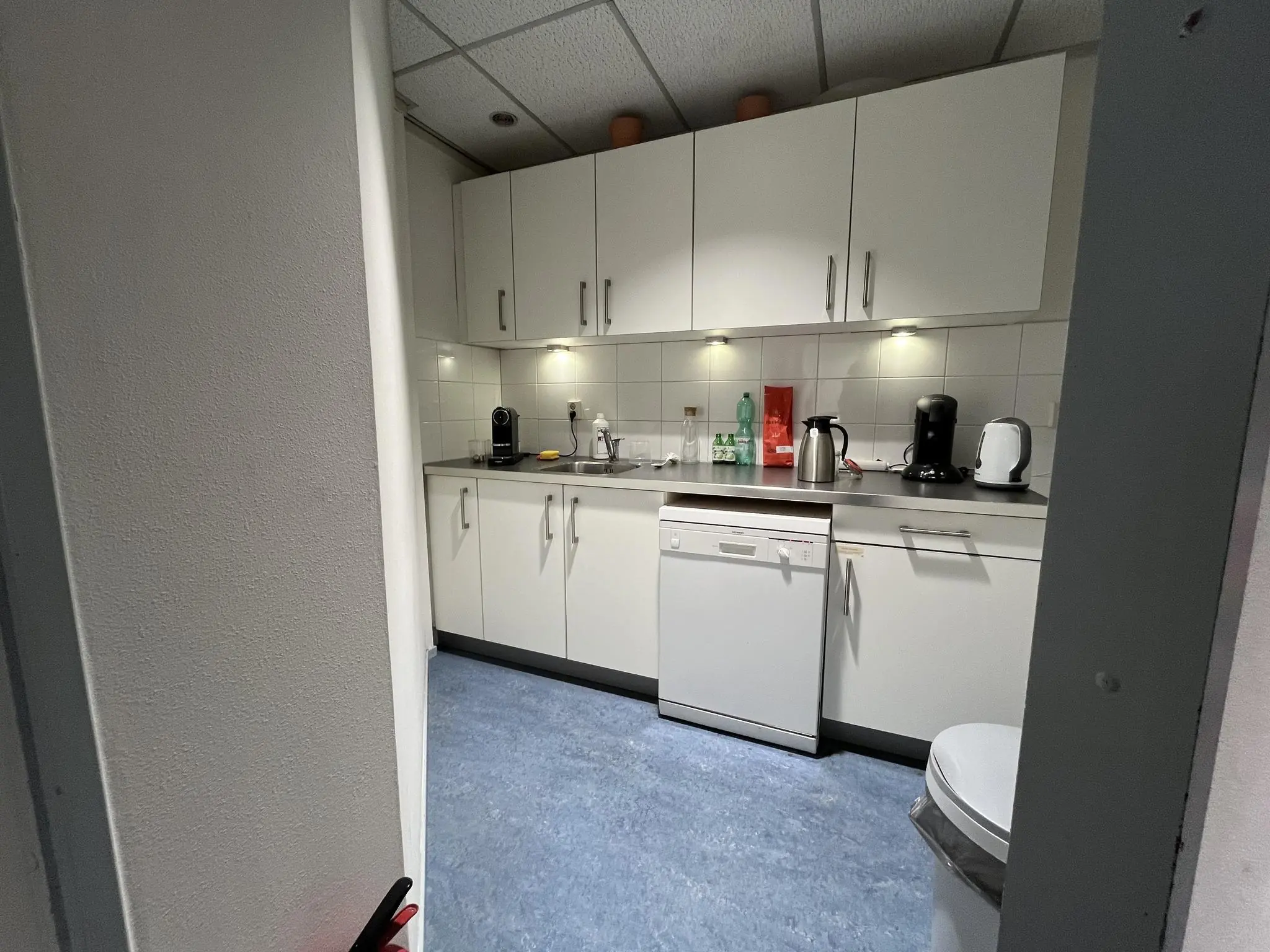 Kleine bedrijfskeuken met witte kasten, keukenapparatuur en een vaatwasser aan de Industrieweg.