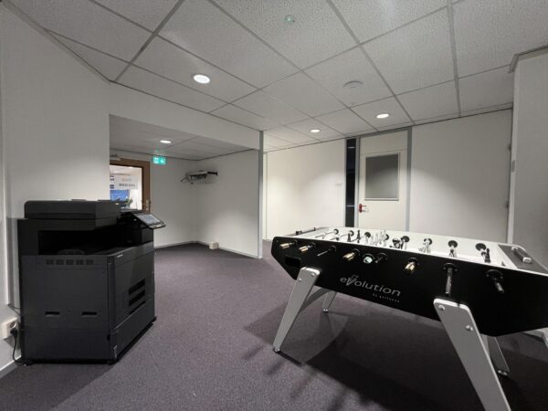Kantoorruimte met een tafelvoetbaltafel en een grote multifunctionele printer.