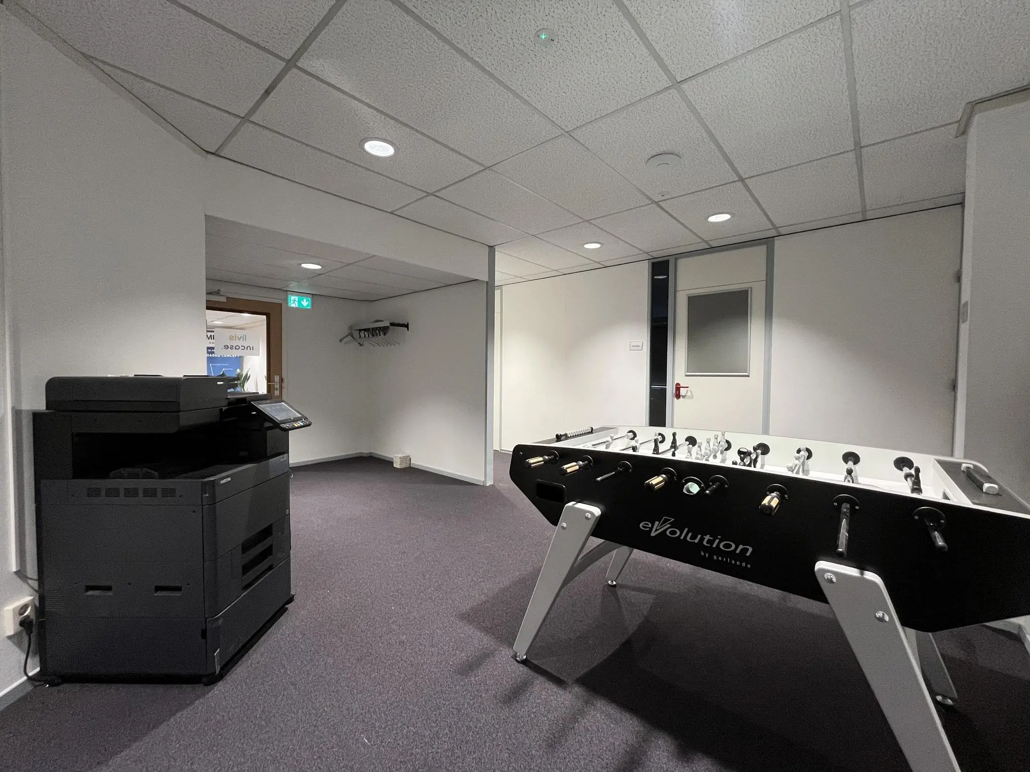 Kantoorruimte met een tafelvoetbaltafel en een grote multifunctionele printer.