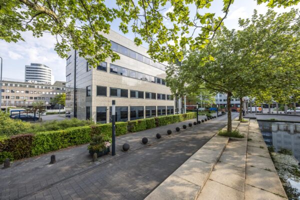 Modern kantoorgebouw aan de Varrolaan in Utrecht, met bomen en vijver op de voorgrond.