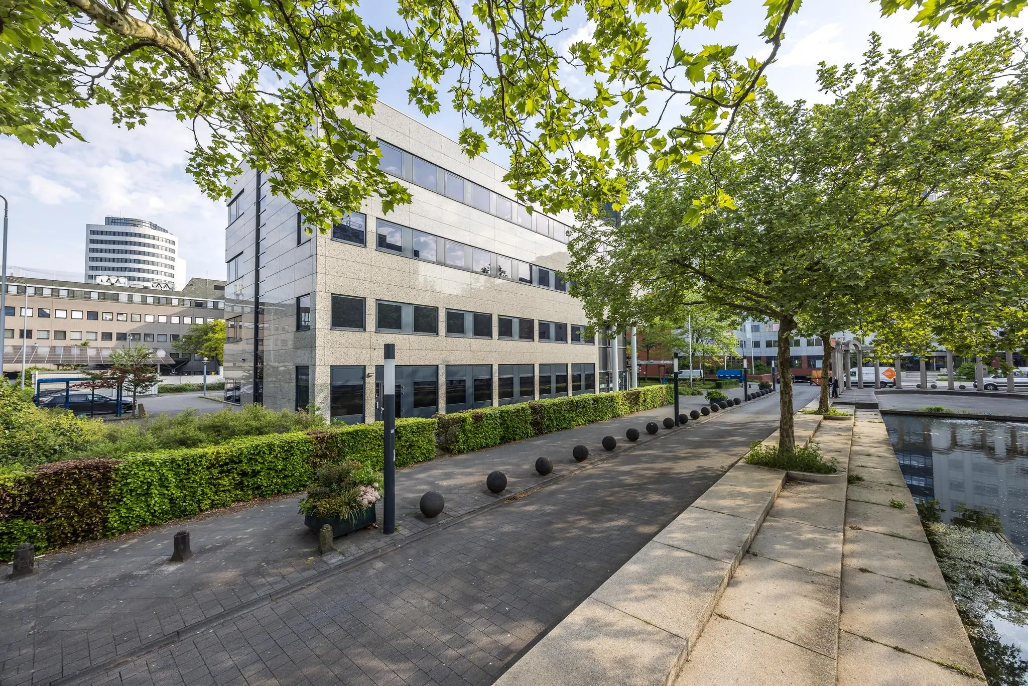 Modern kantoorgebouw aan de Varrolaan in Utrecht, met bomen en vijver op de voorgrond.