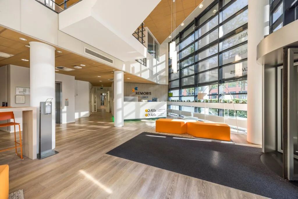 Moderne en ruime entreehal van het kantoorgebouw aan de Varrolaan, met oranje zitmeubels en veel natuurlijk licht.