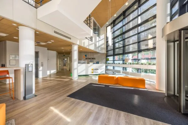 Moderne en ruime entreehal van het kantoorgebouw aan de Varrolaan, met oranje zitmeubels en veel natuurlijk licht.