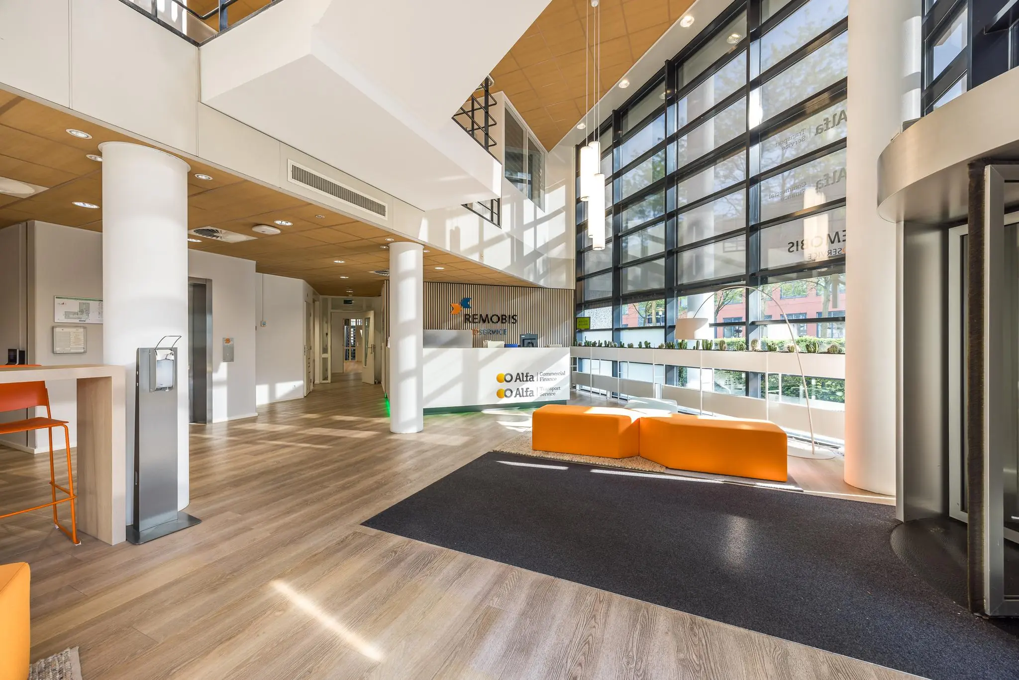 Moderne en ruime entreehal van het kantoorgebouw aan de Varrolaan, met oranje zitmeubels en veel natuurlijk licht.