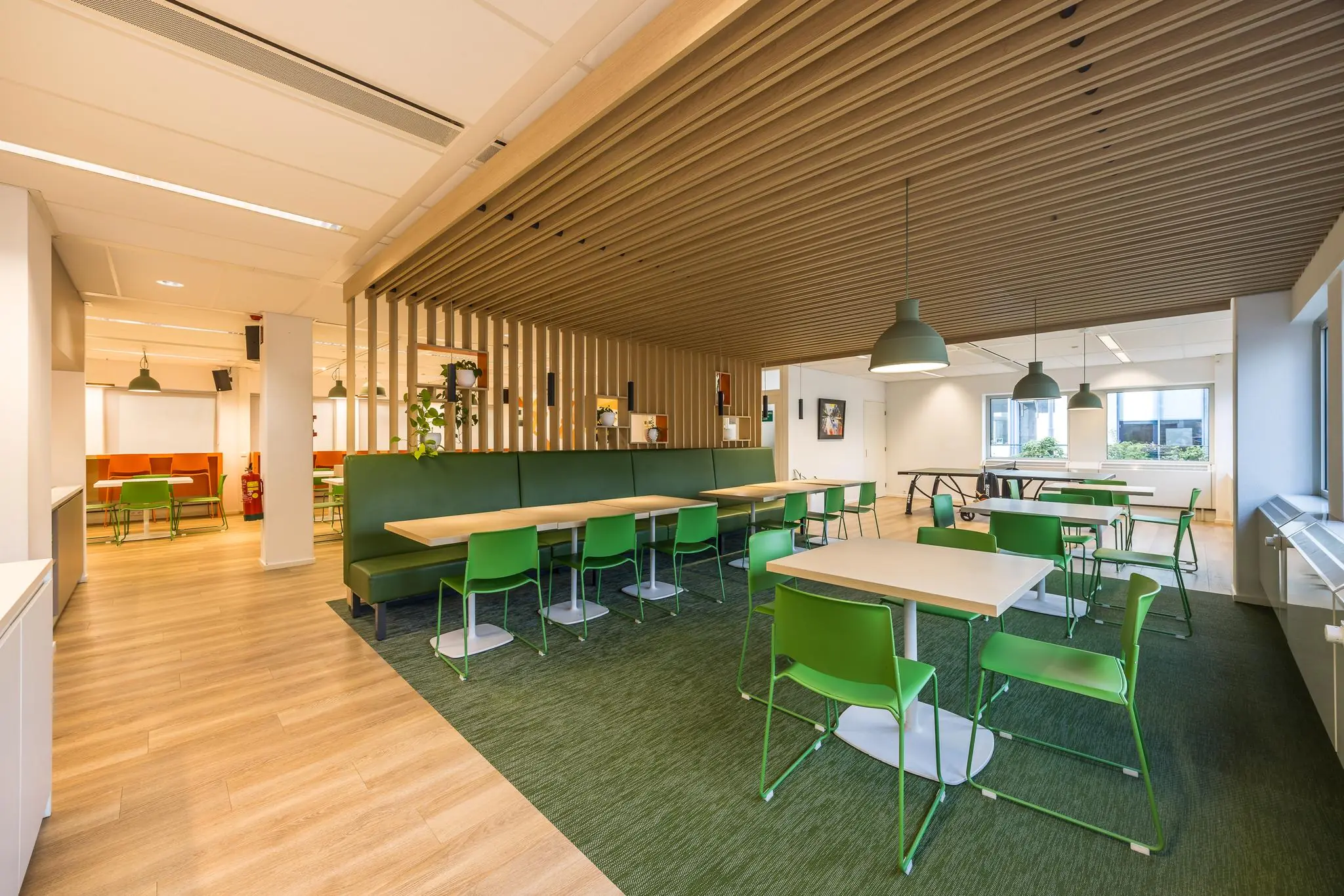 Modern ingerichte kantine aan de Varrolaan met groene stoelen, houten accenten en veel natuurlijk licht.