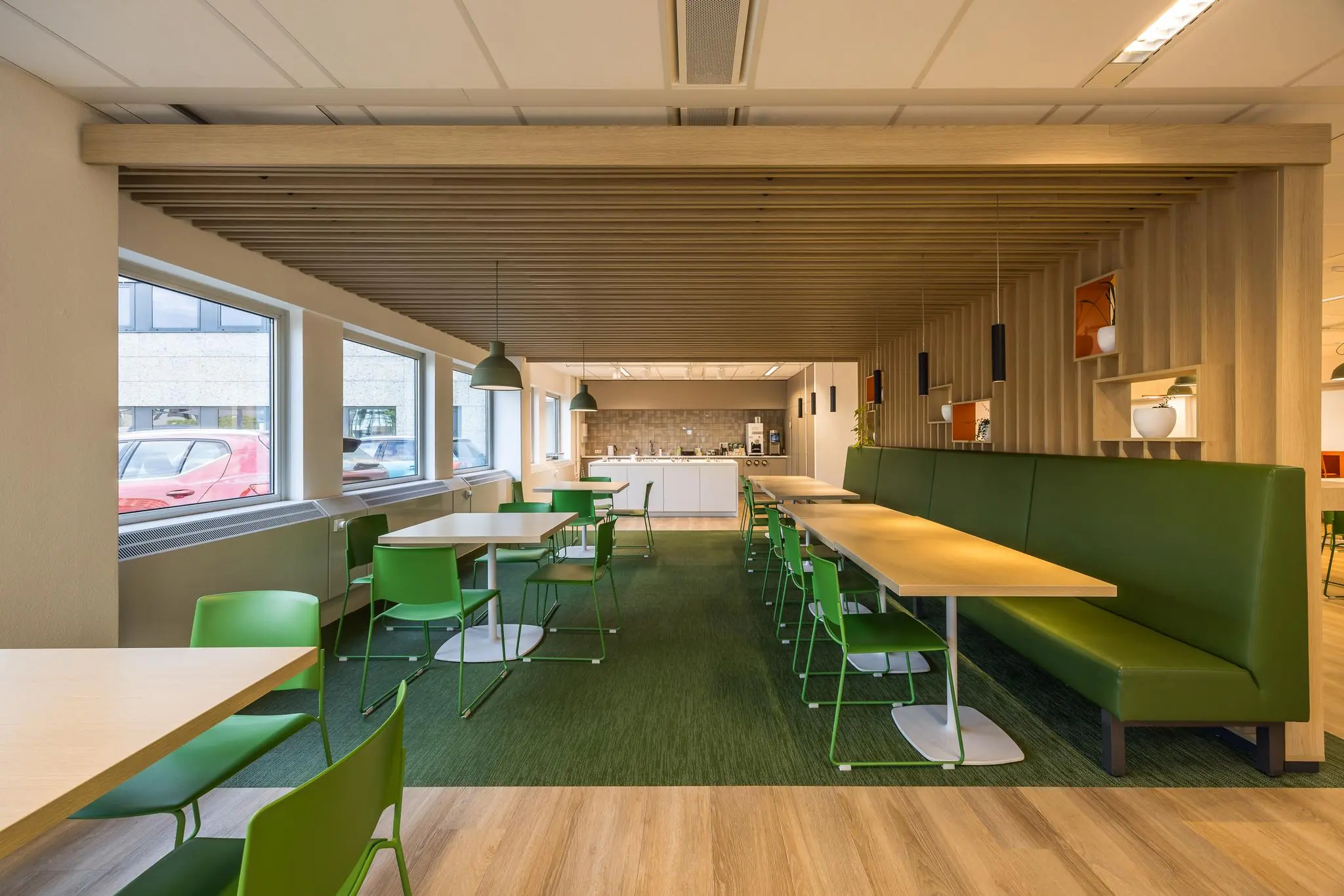 Moderne kantineruimte aan de Varrolaan met groene stoelen, houten accenten en een open keuken.