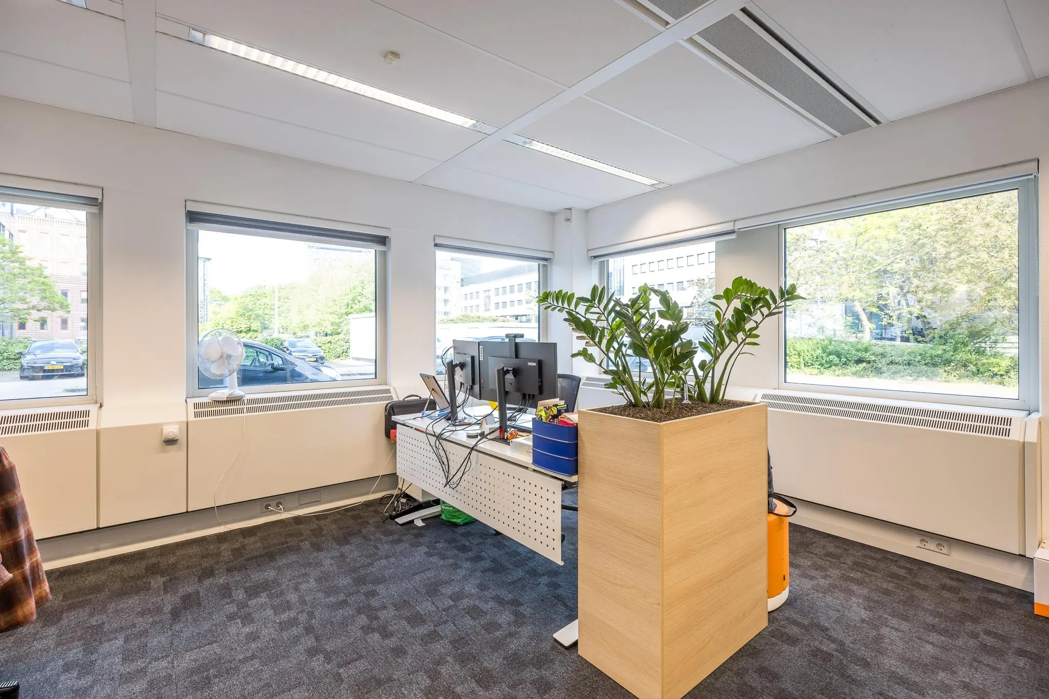 Modern kantoor met werkplek, grote ramen, computerschermen en een plantenbak aan de Varrolaan.